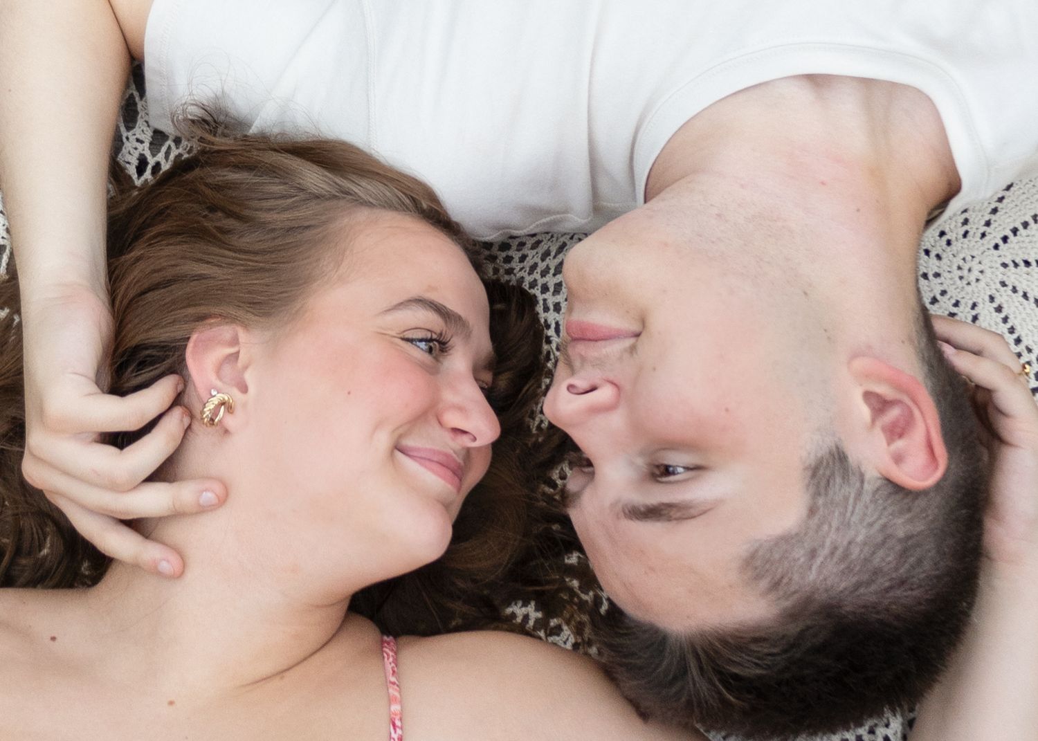 Couple lying down face to face smiling and gazing lovingly at each other in natural light.