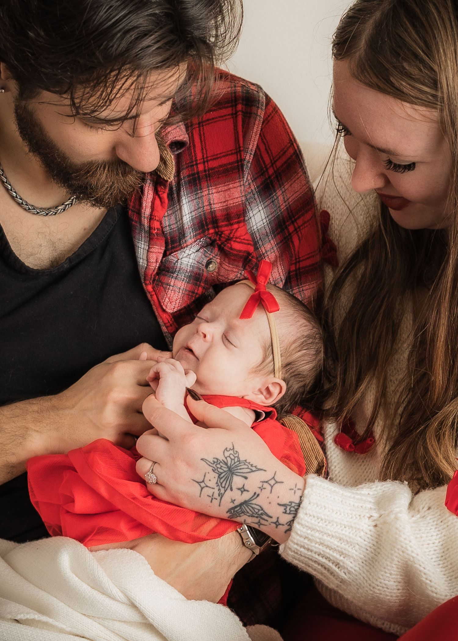 New parents tenderly admire their sleeping newborn dressed in red holiday outfit.