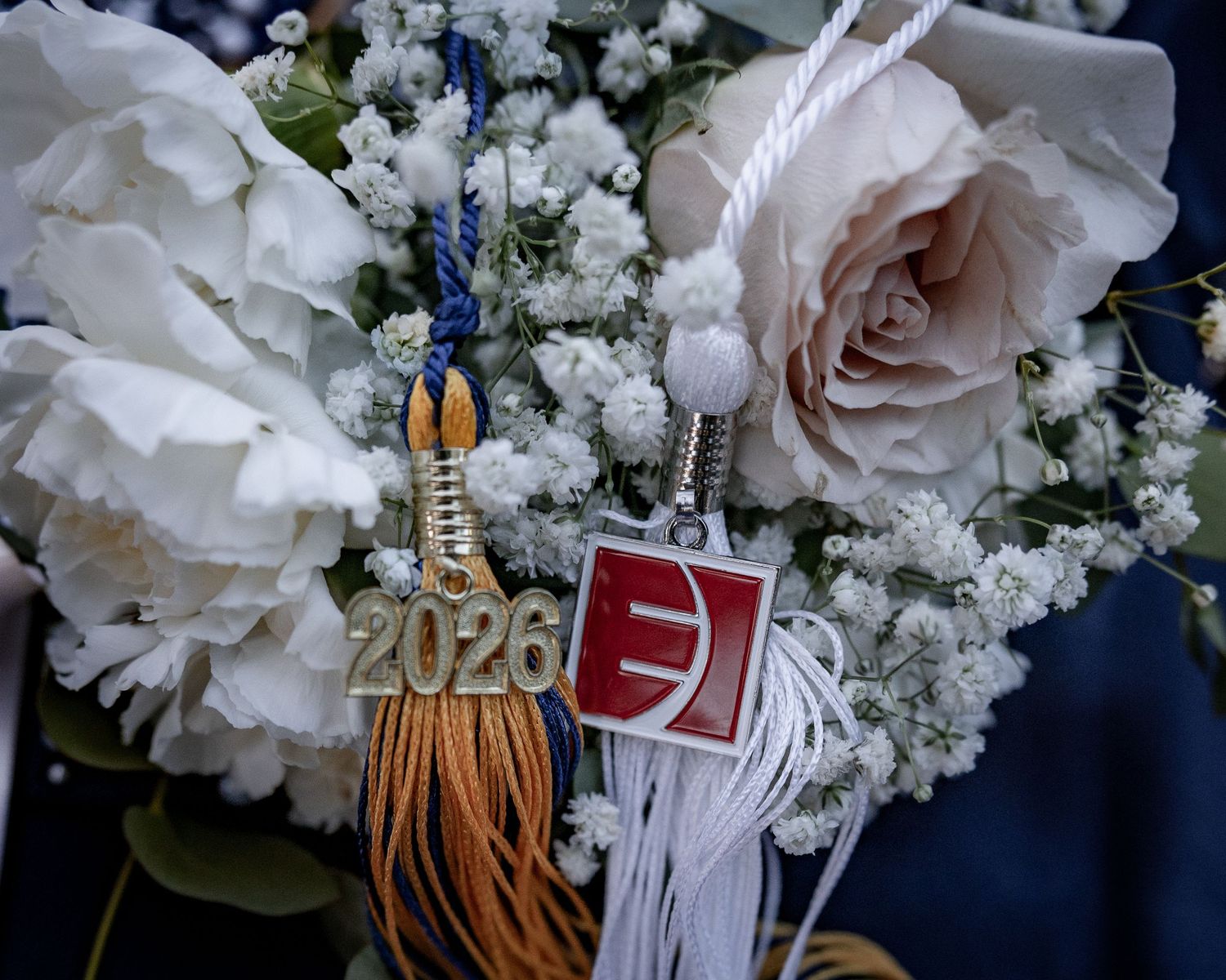 Class of 2026 graduation tassel and charm displayed with white roses and baby's breath bouquet.