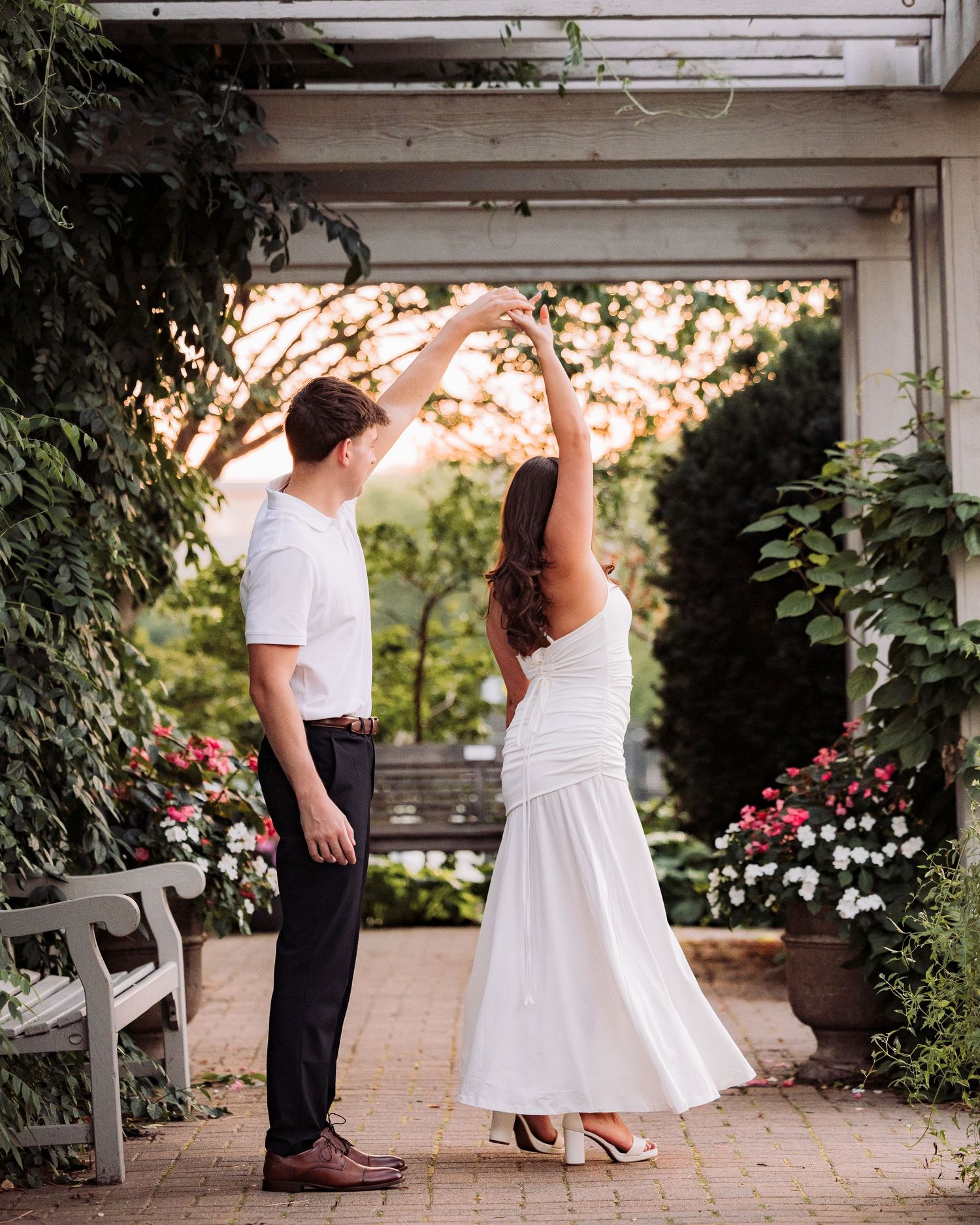 Couple dancing outdoors in a garden, woman in white dress being twirled by man in white shirt and black pants.