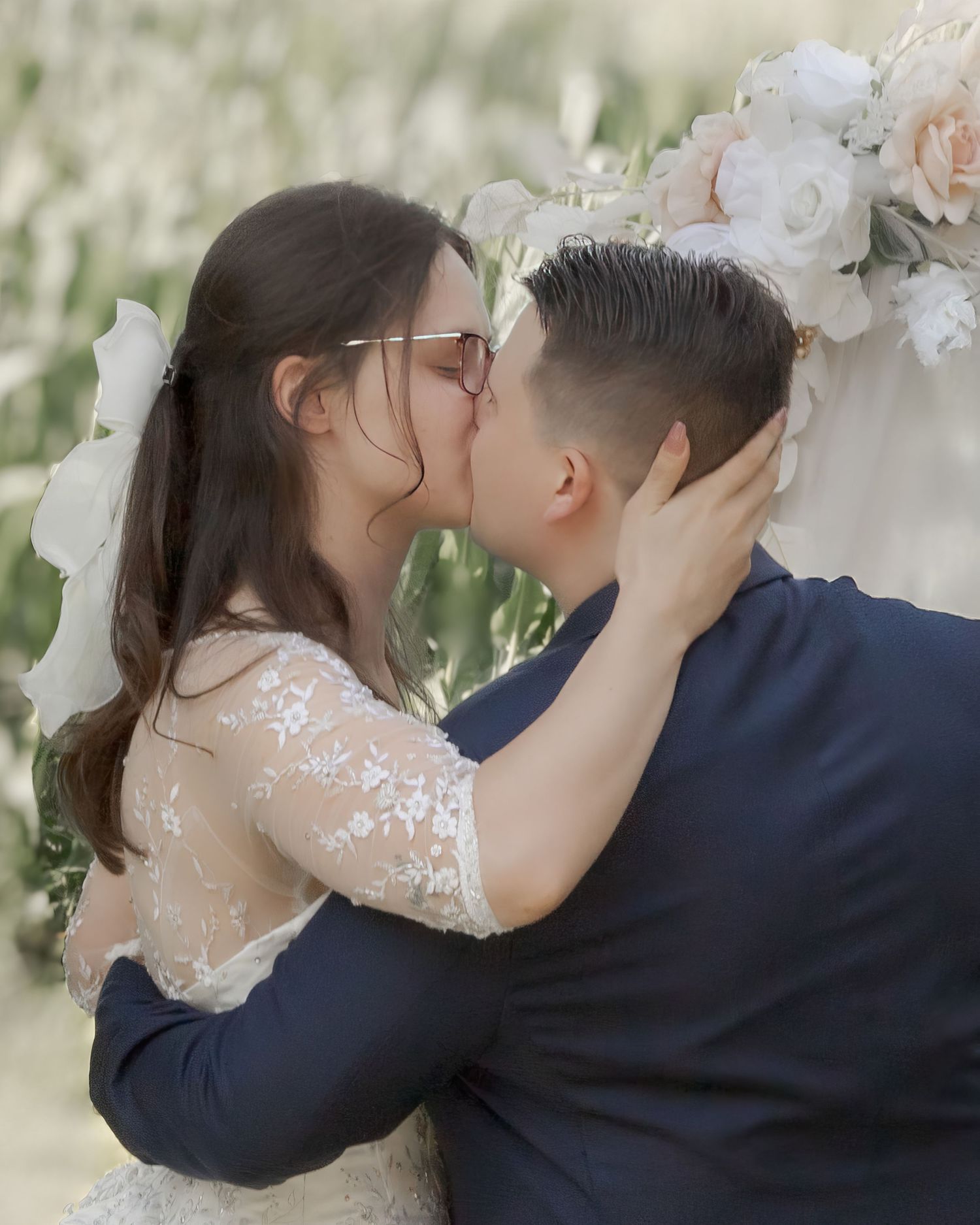 Bride and groom share their first kiss under a floral arch at outdoor wedding.