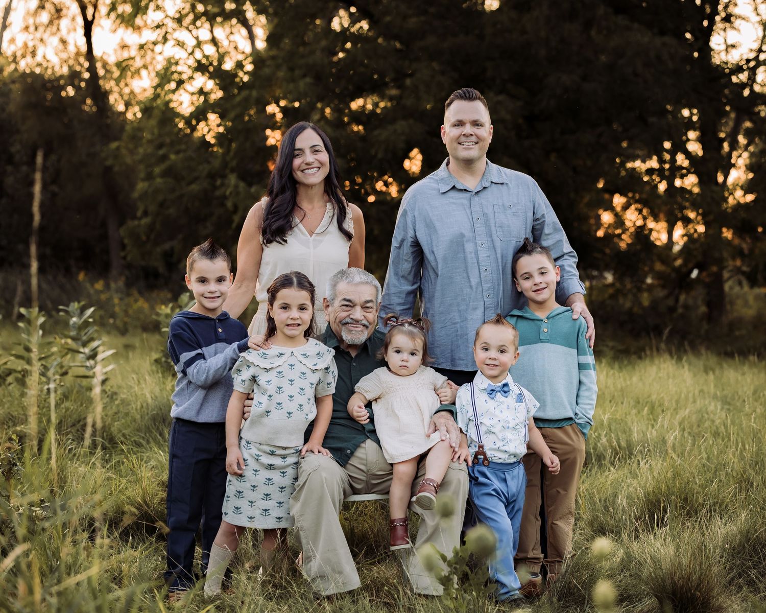 Multi-generational family posing together in a sunlit meadow at golden hour, featuring grandparents, parents, and five young children.