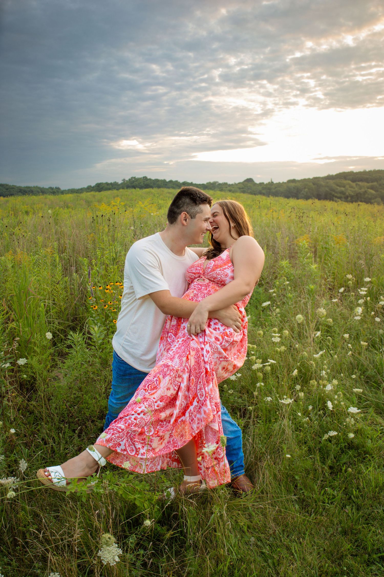Couple embracing and sharing a romantic moment in a green meadow, woman in pink floral dress at dusk.