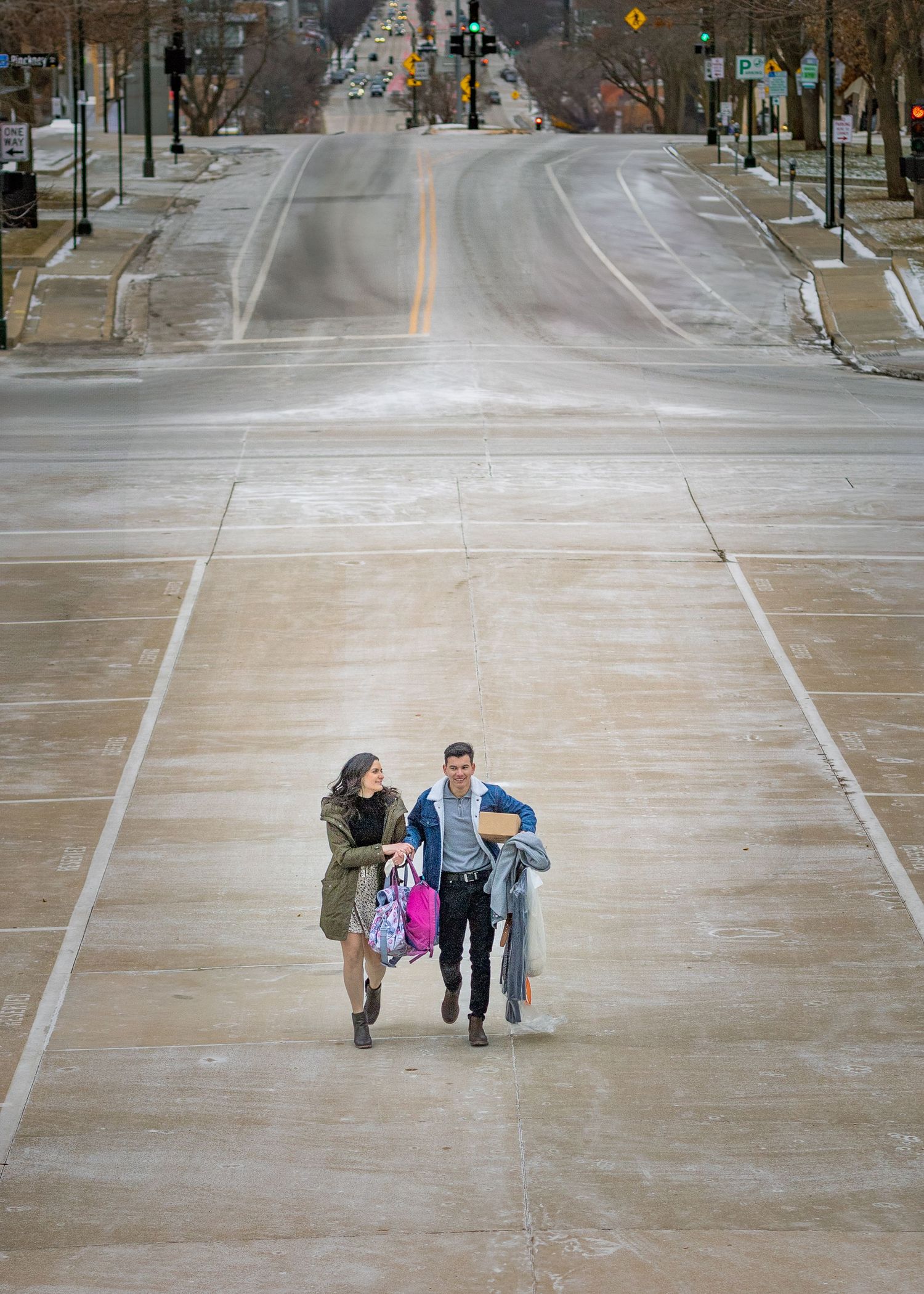 Aerial view of couple walking up wide empty urban plaza with city street stretching behind them.