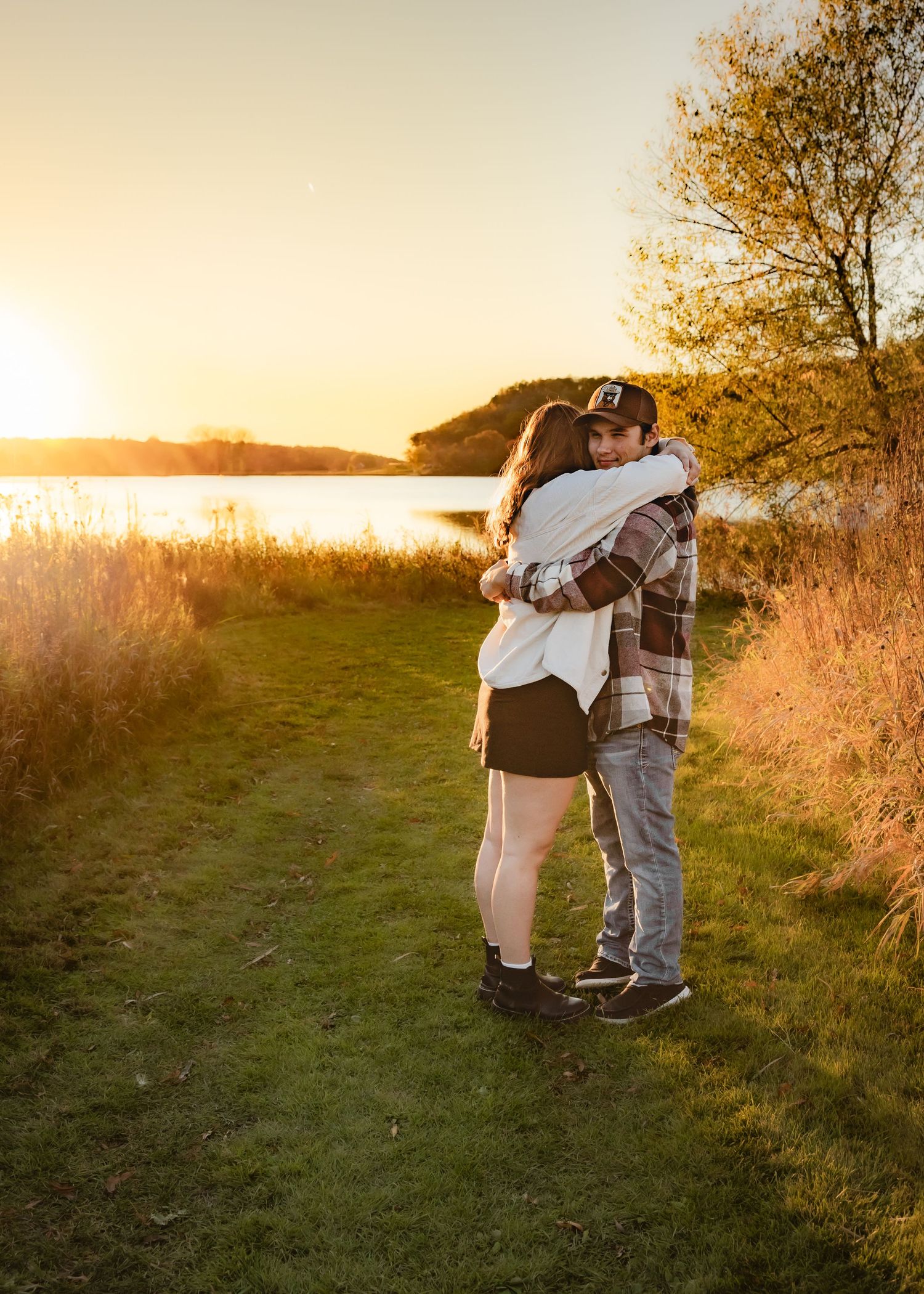 Couple embracing in a warm hug by a peaceful lake during a beautiful sunset.