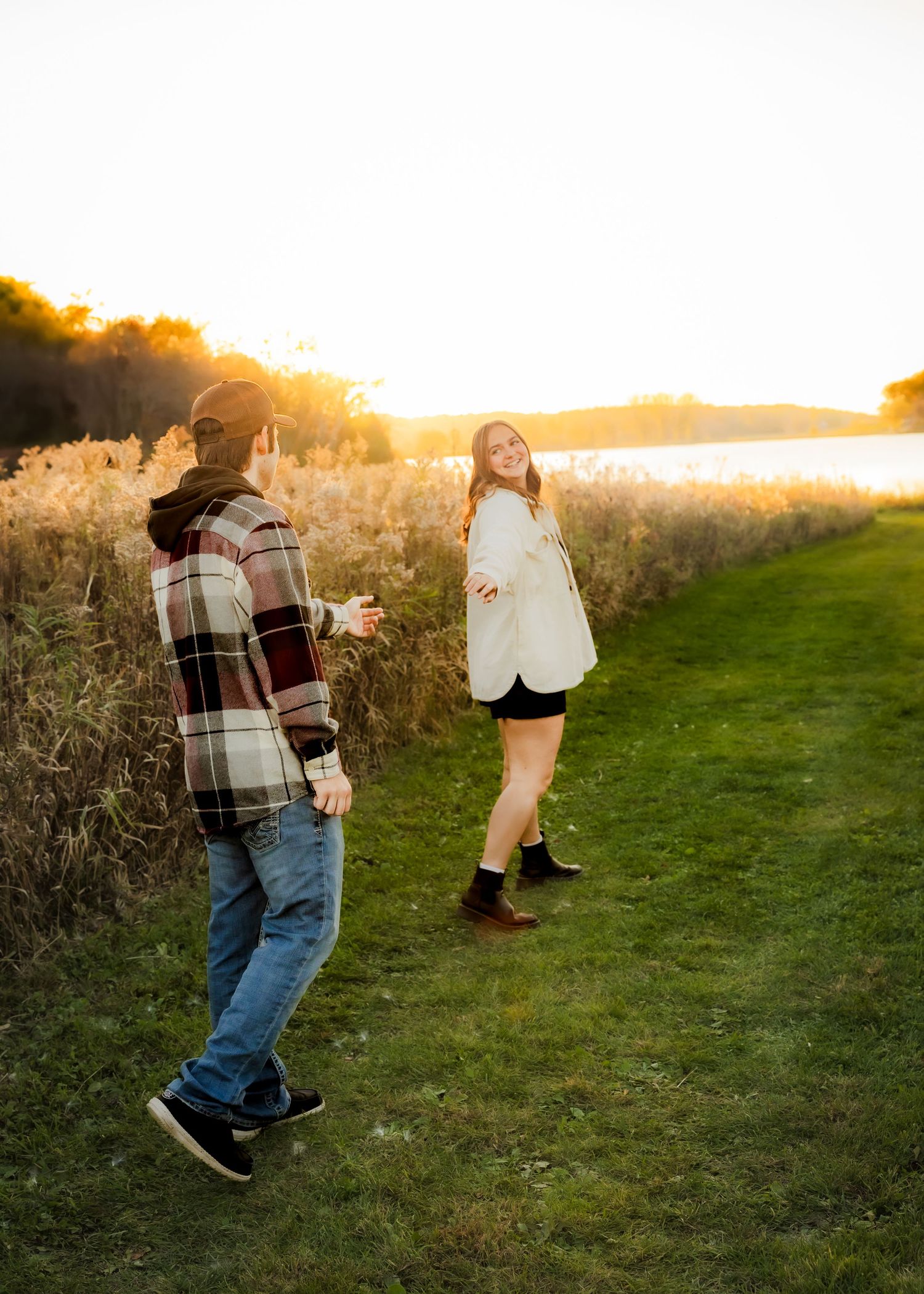 Couple walking along a lakeside path at sunset, woman smiling back over her shoulder.