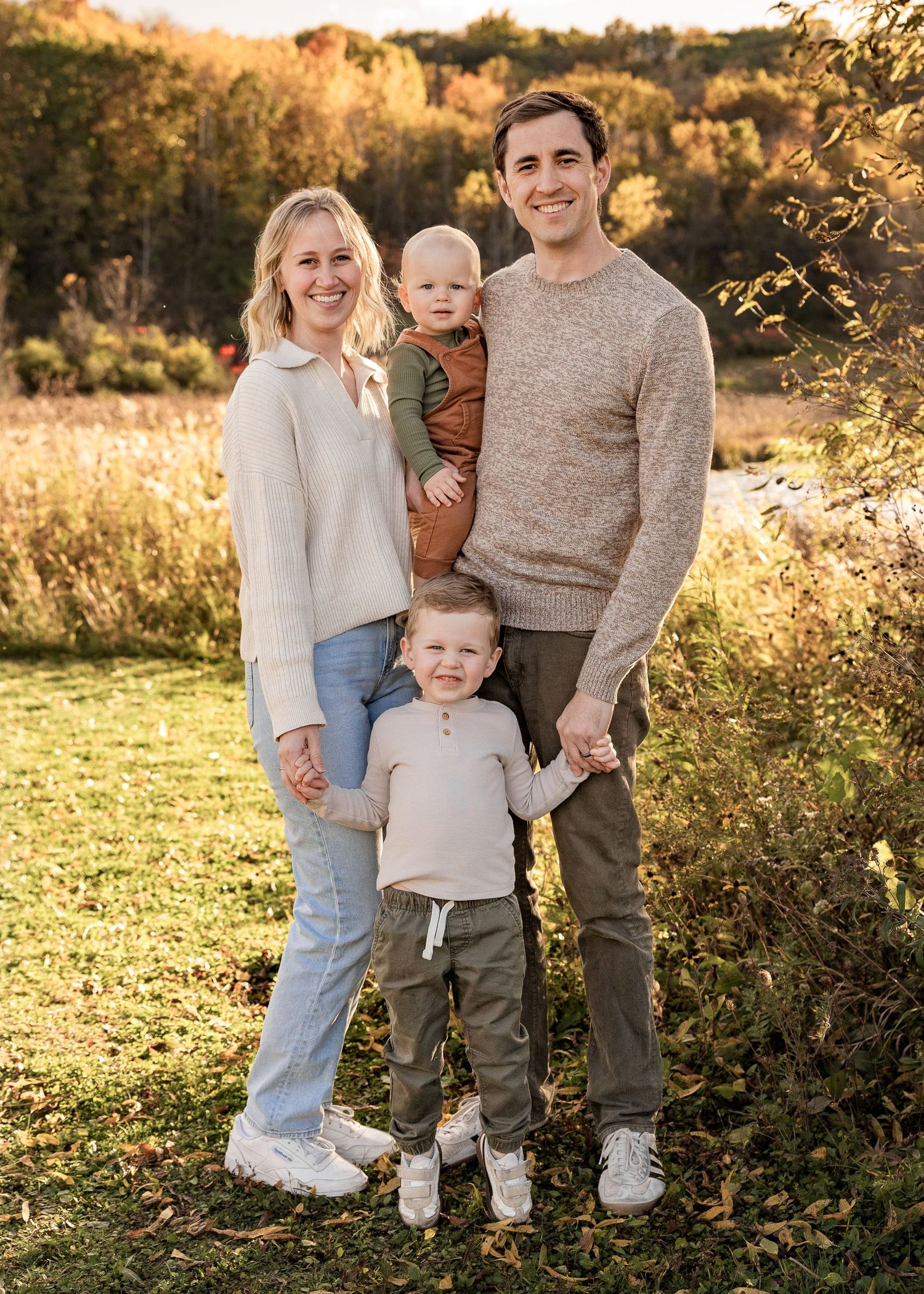 Happy family of four posing together in a golden autumn meadow during fall family photos.