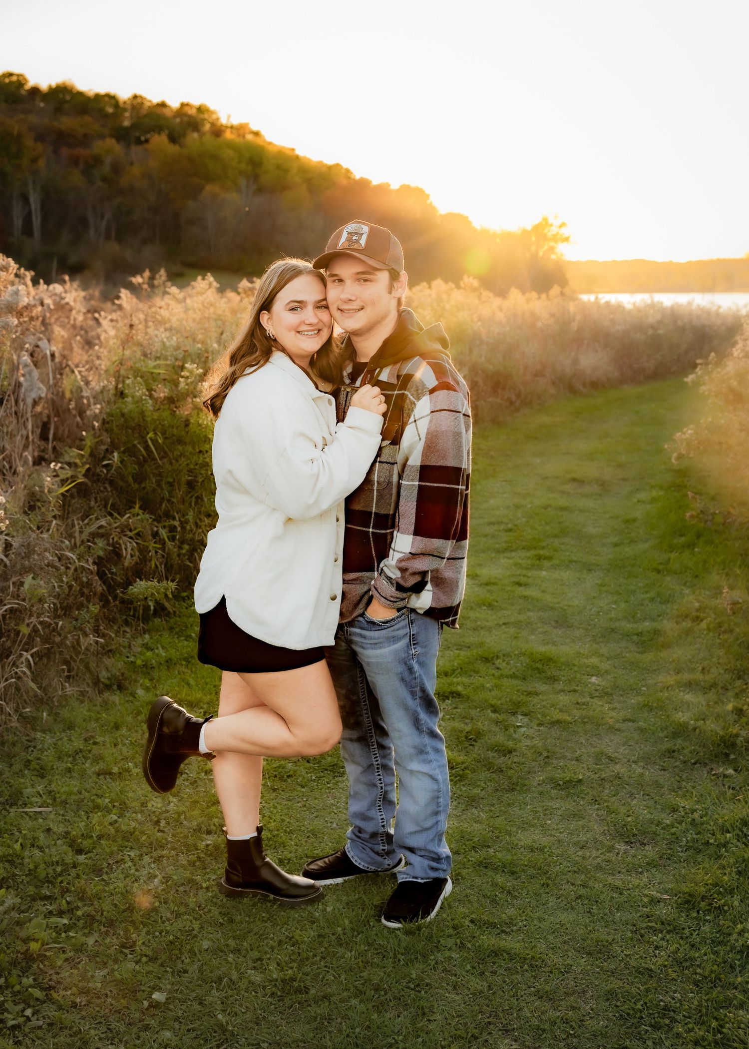 Smiling couple embracing on scenic path near lake during beautiful golden hour sunset.