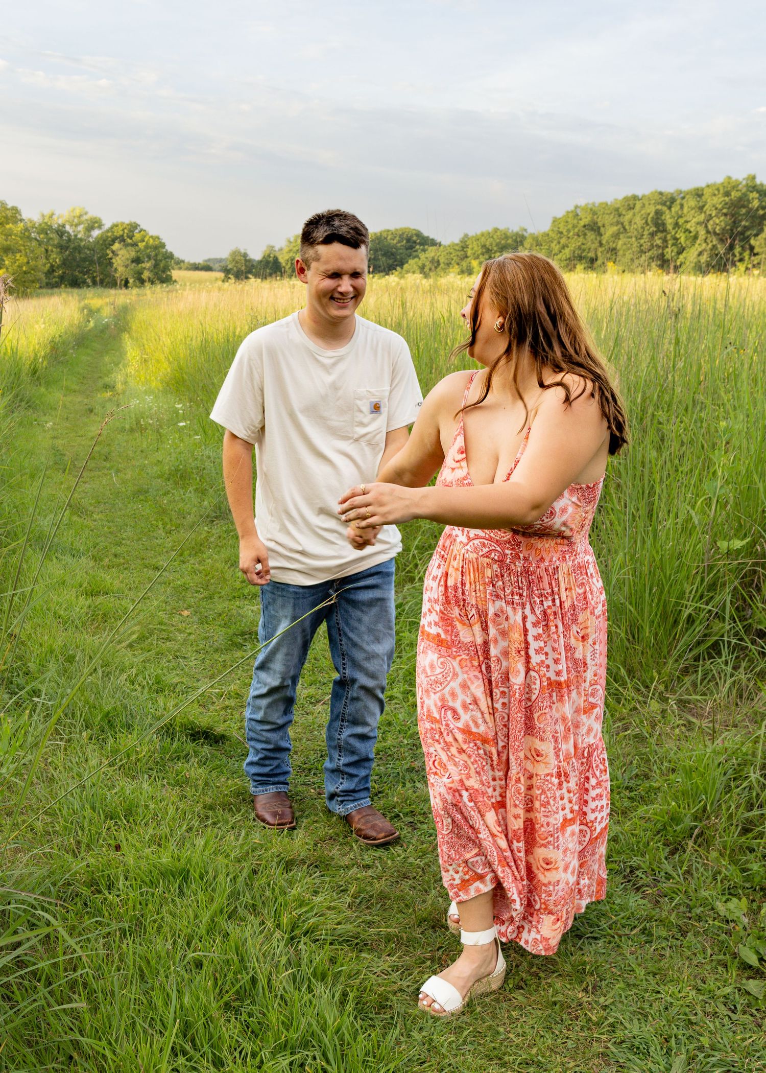 Happy couple holding hands and laughing together on a green meadow path on a bright summer day.