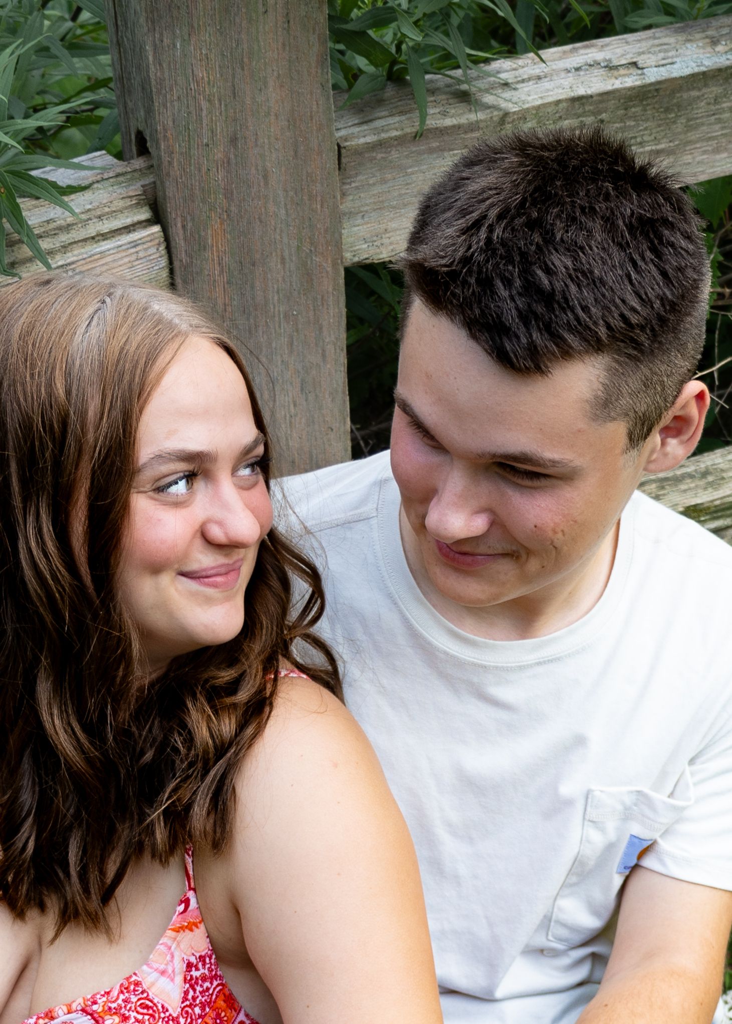Young couple sitting on wooden steps smiling at each other in a lush green setting.