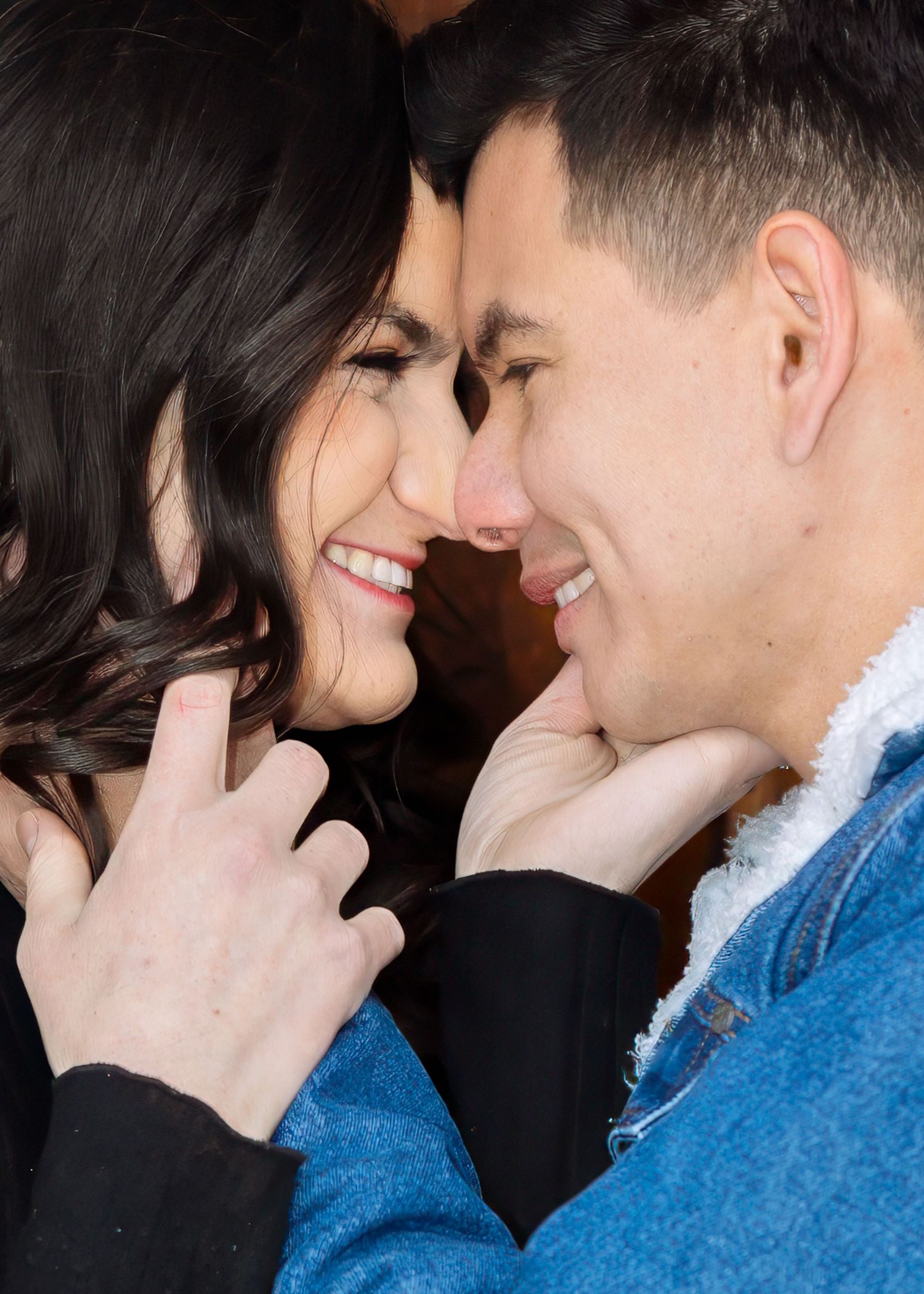 Close-up of joyful couple nearly nose-to-nose, woman in black top and man in denim jacket sharing a romantic moment.