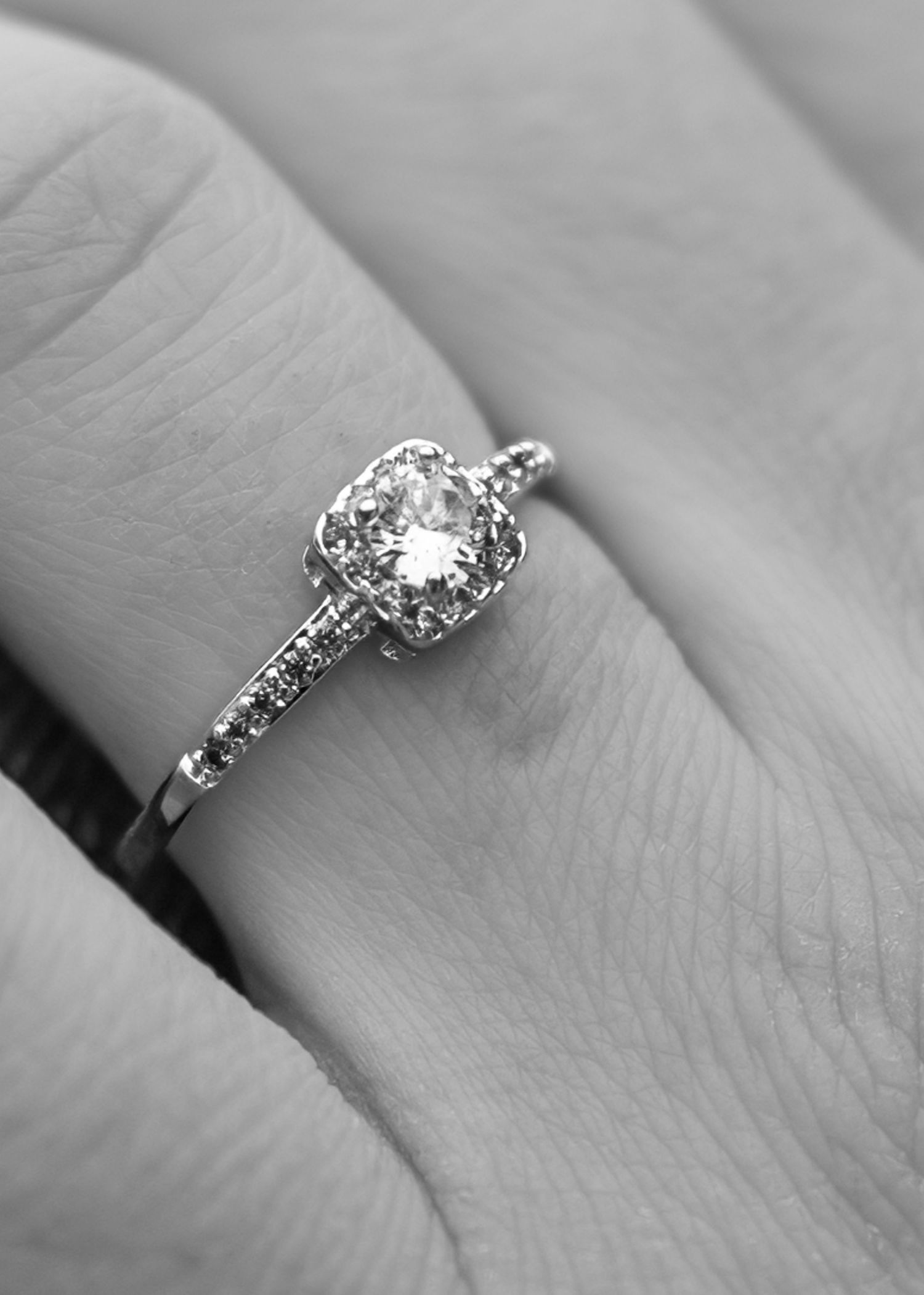 Black and white macro shot of a cushion halo diamond engagement ring on a woman's finger.