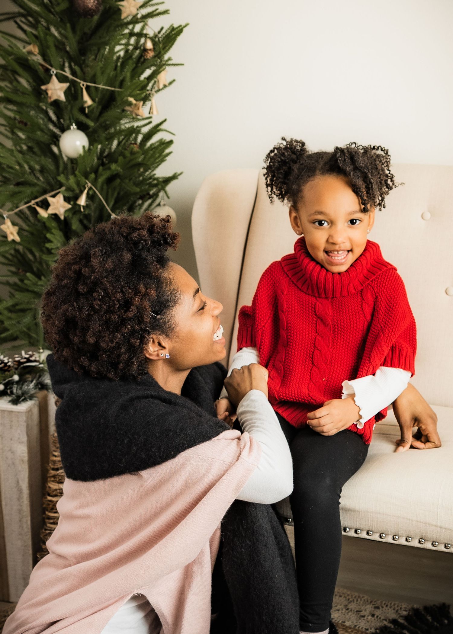 Mother and daughter share a joyful Christmas moment near a decorated holiday tree.
