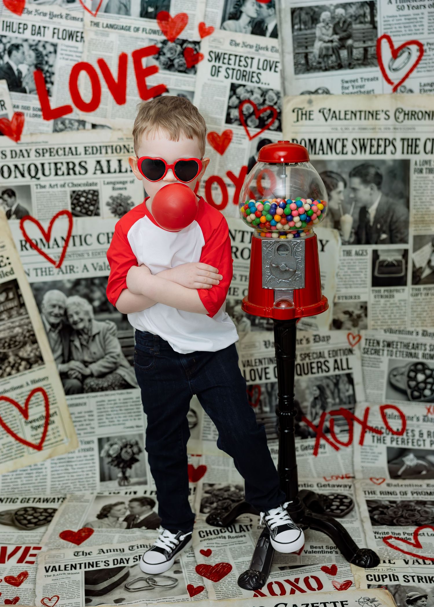 Cool boy in sunglasses blows red bubble gum near gumball machine on Valentine backdrop.