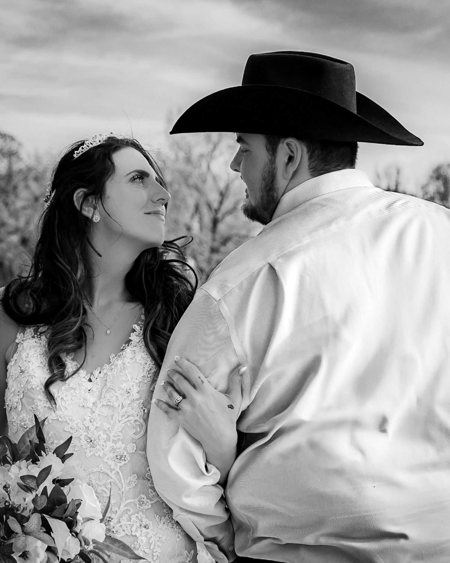 Black and white wedding photo of bride in lace gown and groom in cowboy hat sharing a romantic moment.
