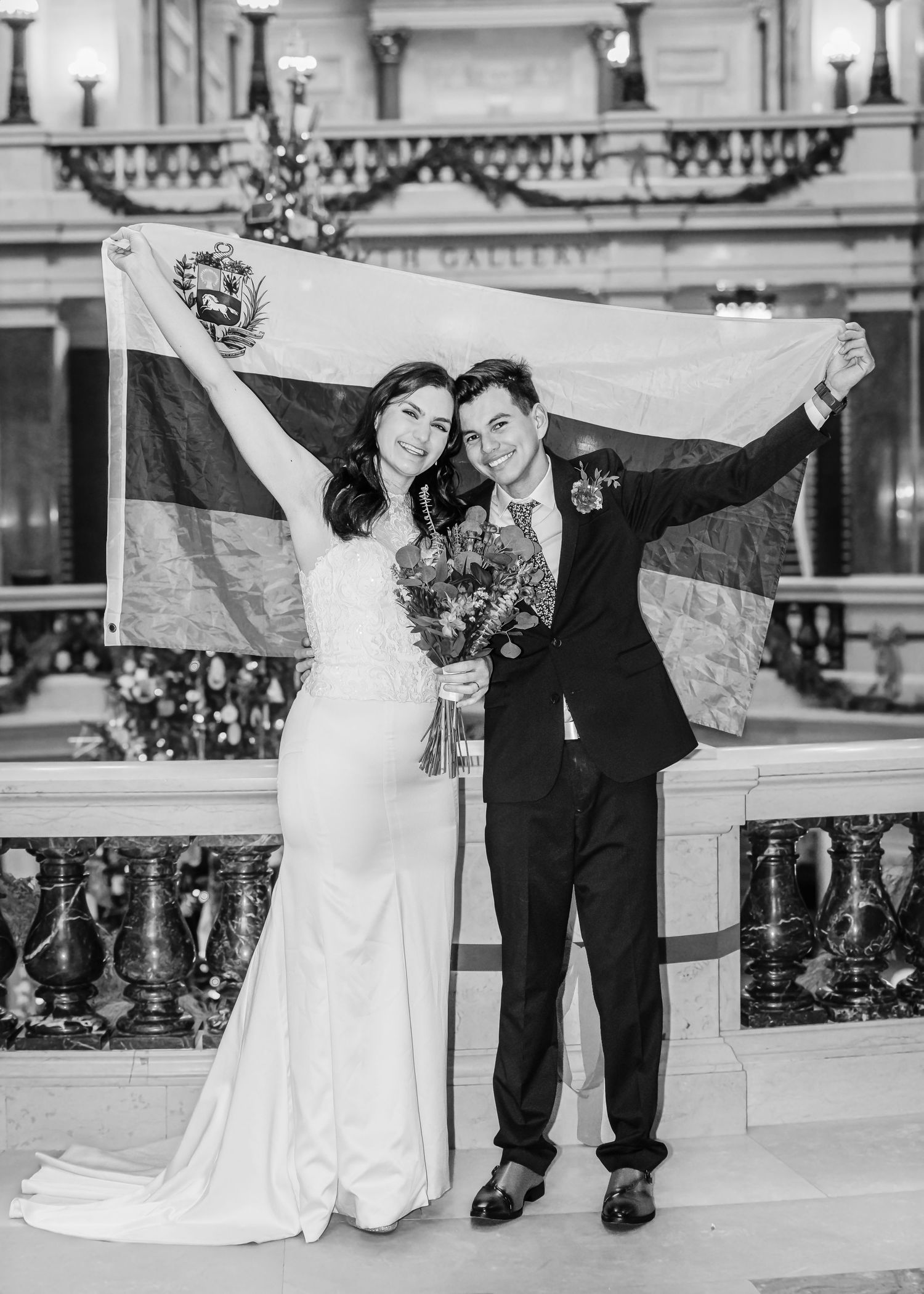Newlyweds celebrate in black and white photo holding flag aloft in ornate wedding venue.