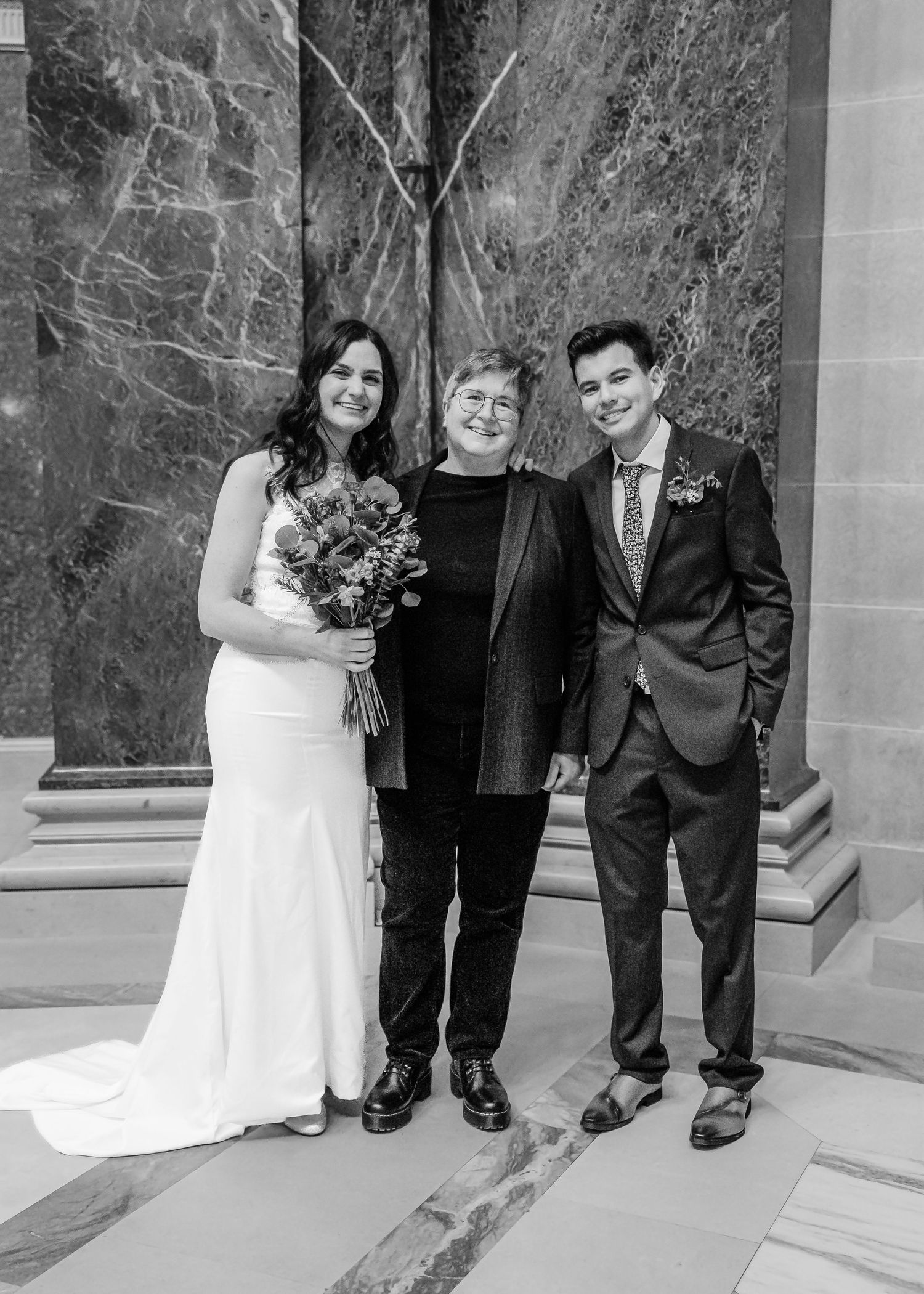 Black and white portrait of bride, officiant, and groom posing together after wedding ceremony.