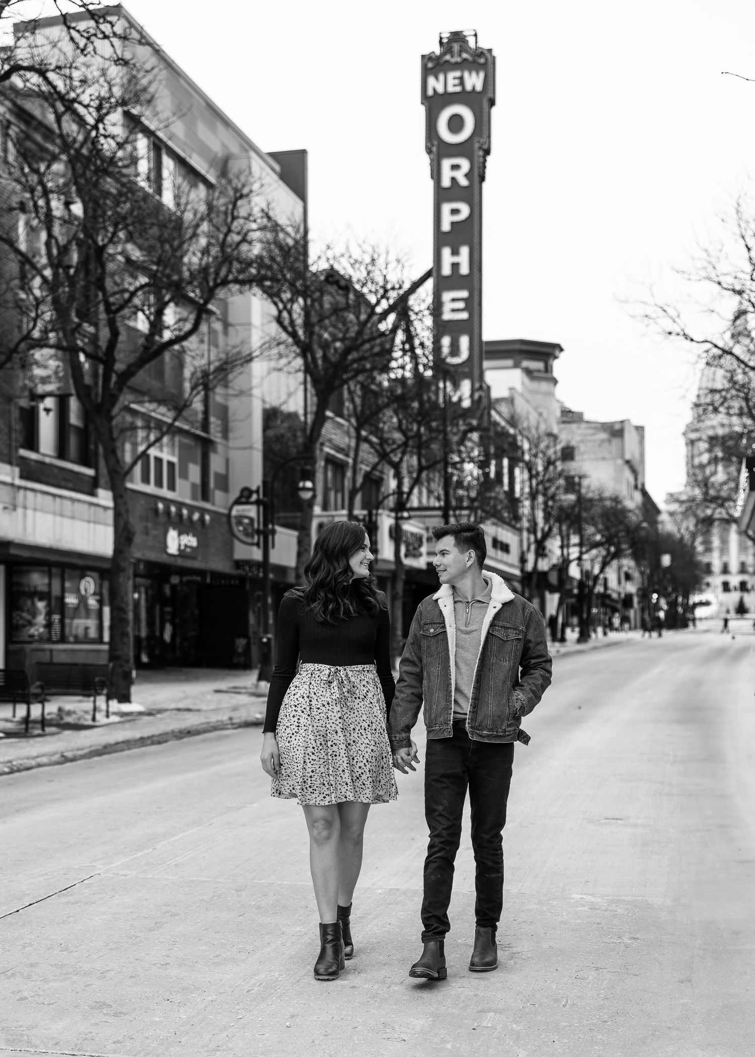 Black and white photo of couple holding hands near New Orpheum Theatre sign on city street.