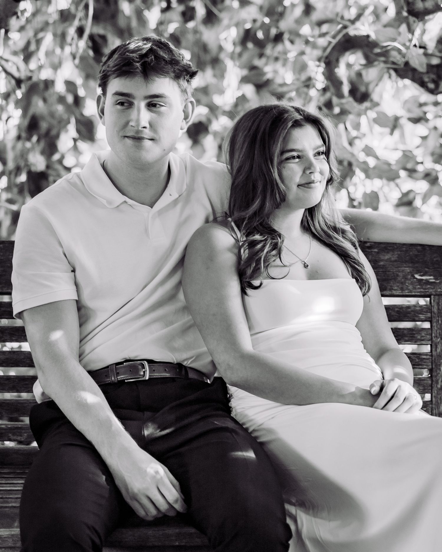 Black and white photo of a young couple sitting together on a bench outdoors, smiling softly.