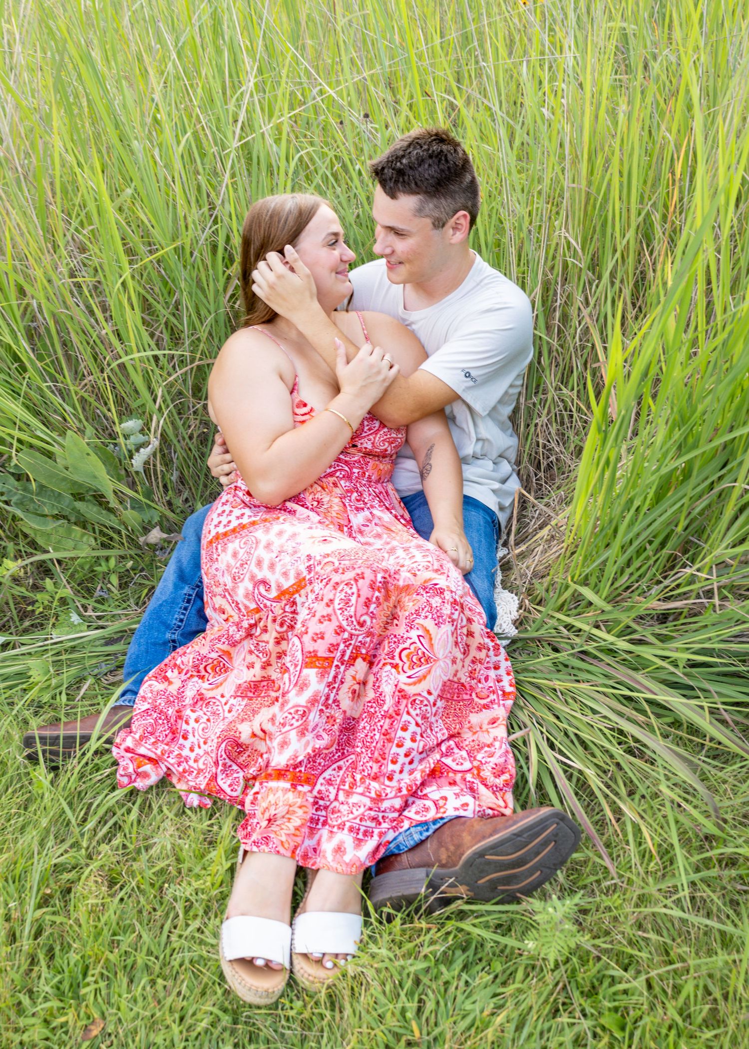 Happy couple sitting together in tall green grass, sharing a joyful moment outdoors.