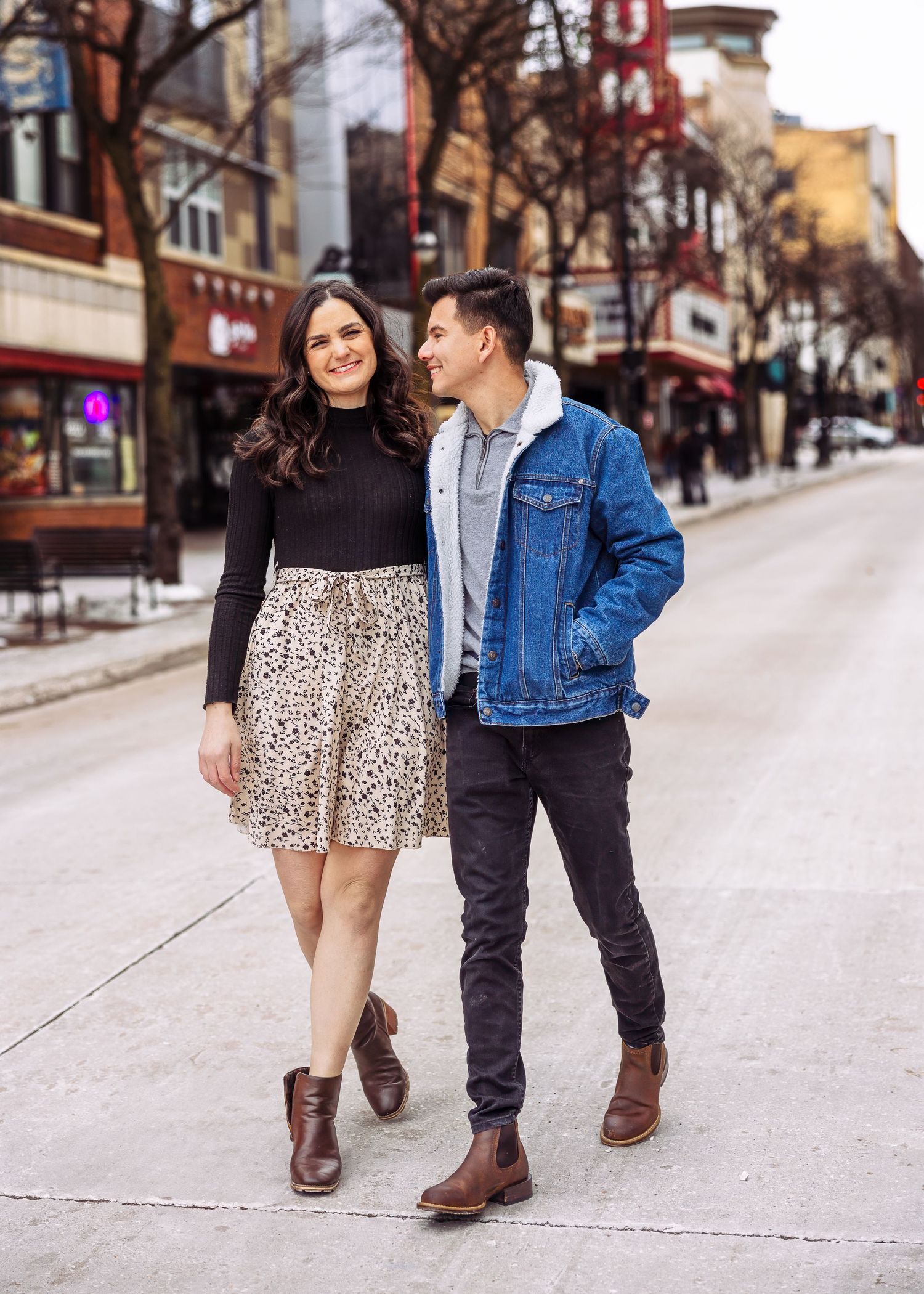 Stylish couple strolling together on a city street with urban storefronts in background.