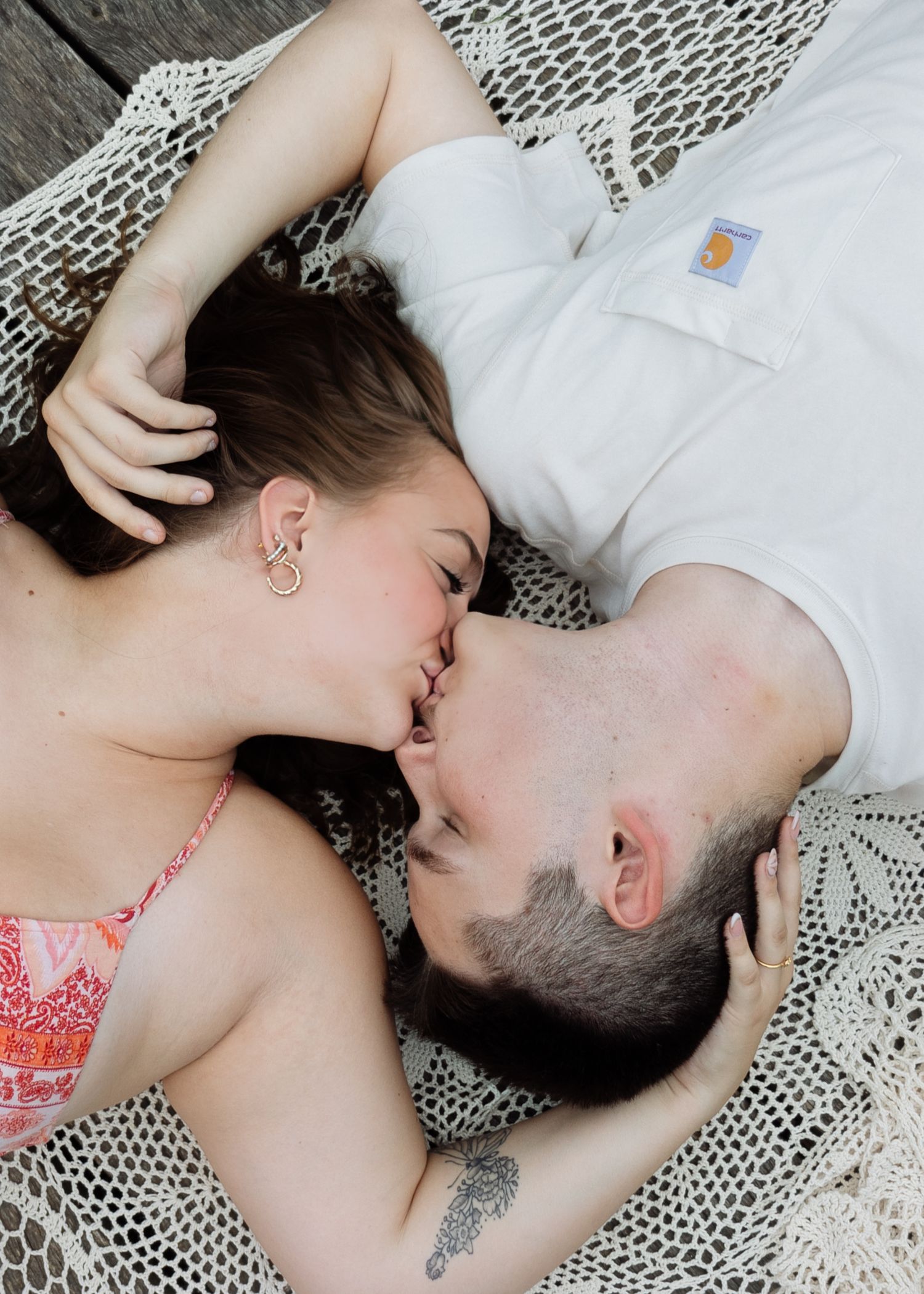 Couple sharing a tender kiss while lying together on a woven blanket in an outdoor setting.