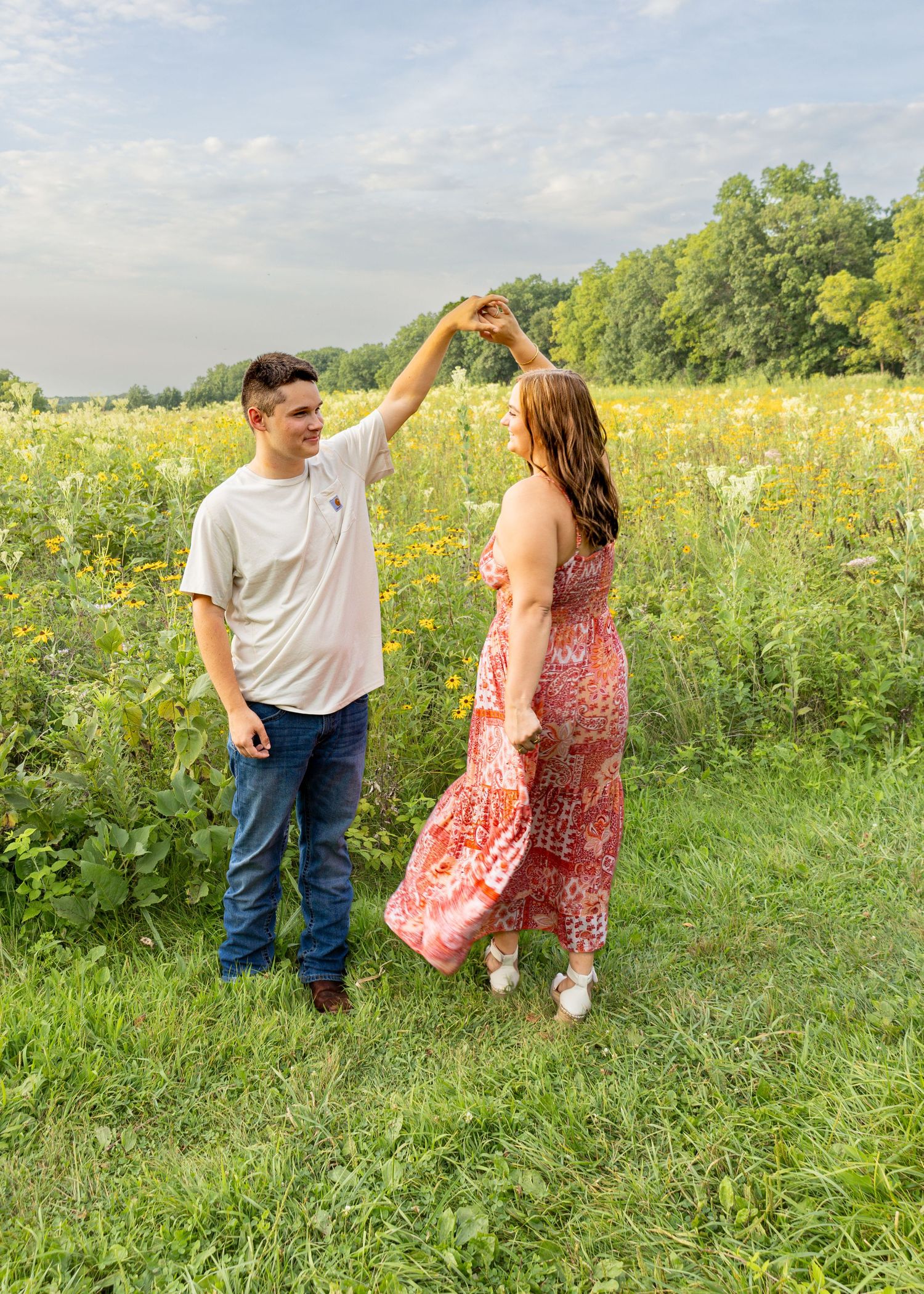 Young couple holding hands and dancing in a vibrant green field with wildflowers.