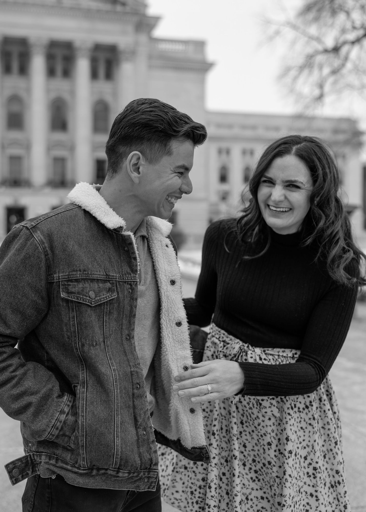 Black and white photo of an engaged couple laughing together outside a grand capitol building.