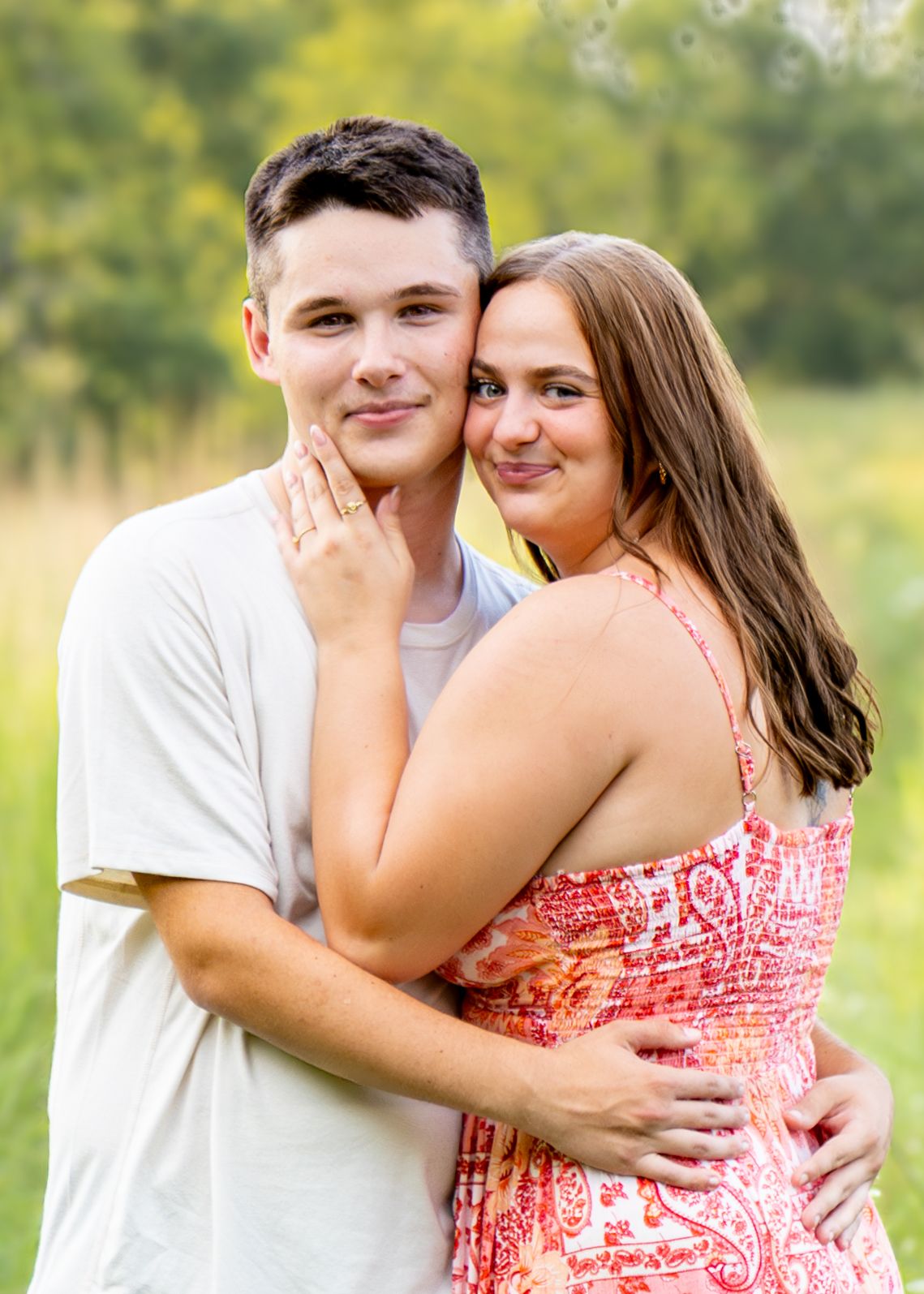 Young couple embracing and smiling together in a sunny green outdoor field setting.
