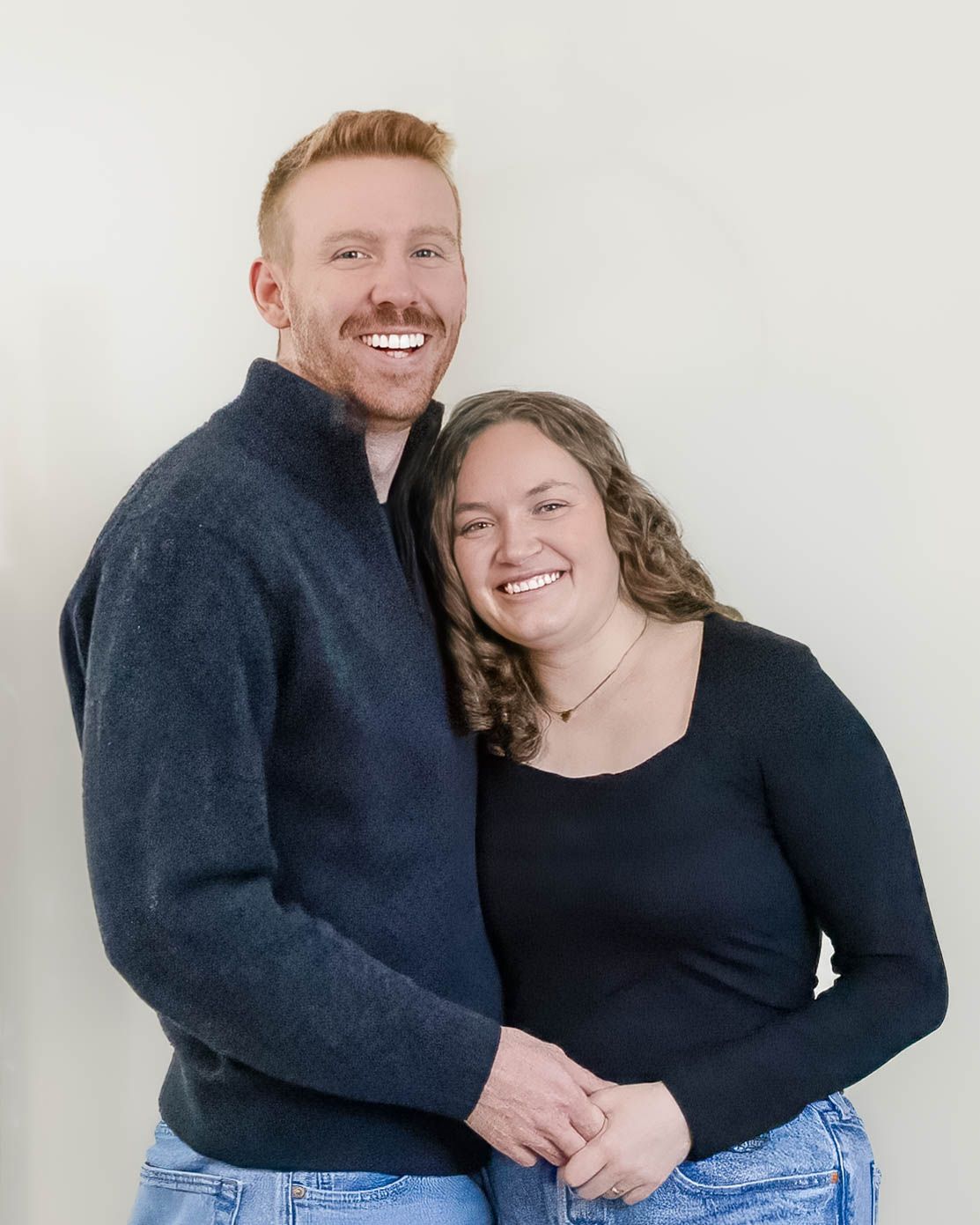 A smiling redheaded man and curly-haired woman pose together in a casual couples portrait.