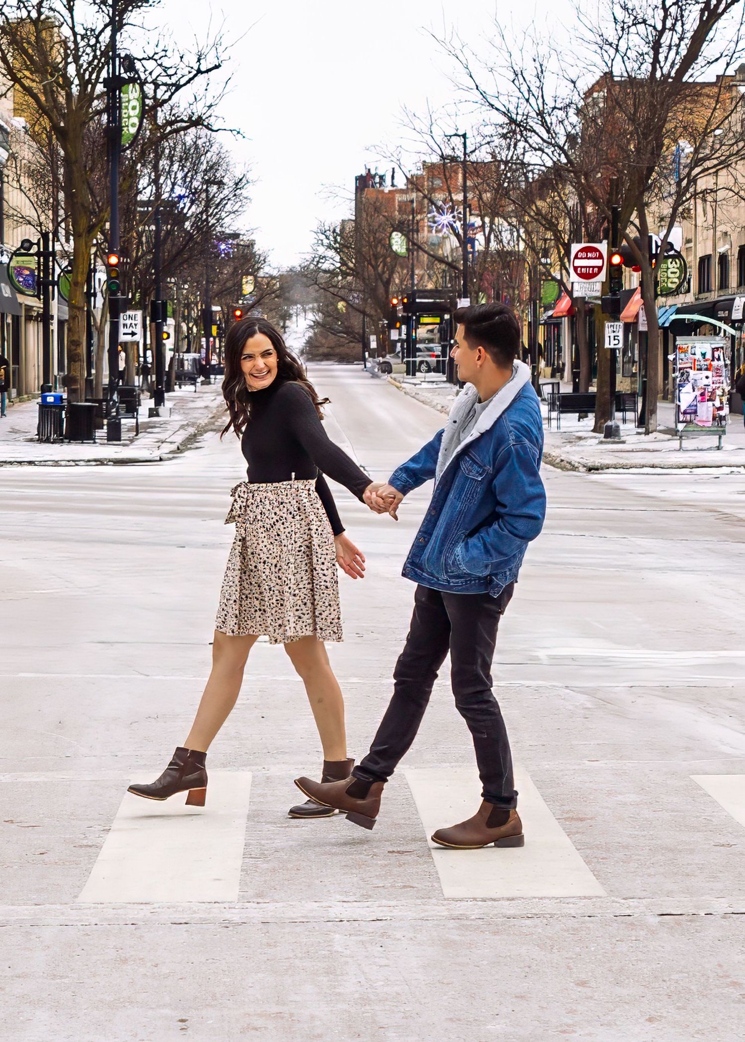 Couple holding hands crossing a zebra crosswalk on a wide urban city street.