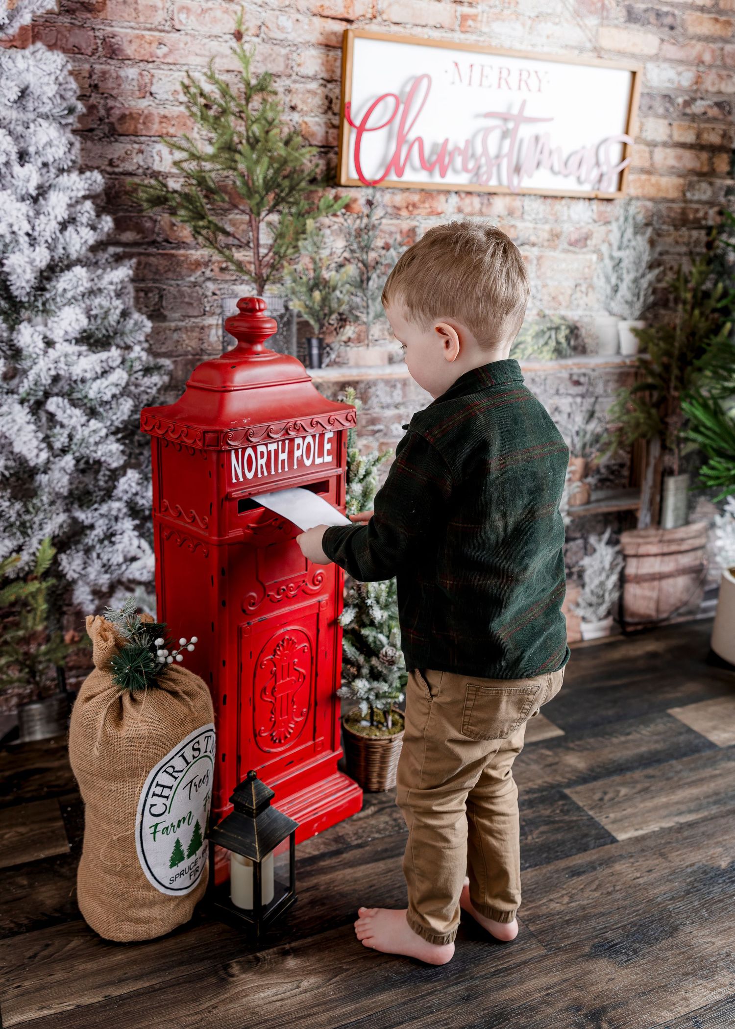 Young boy in green plaid shirt mailing letter at red North Pole mailbox with Christmas decor.