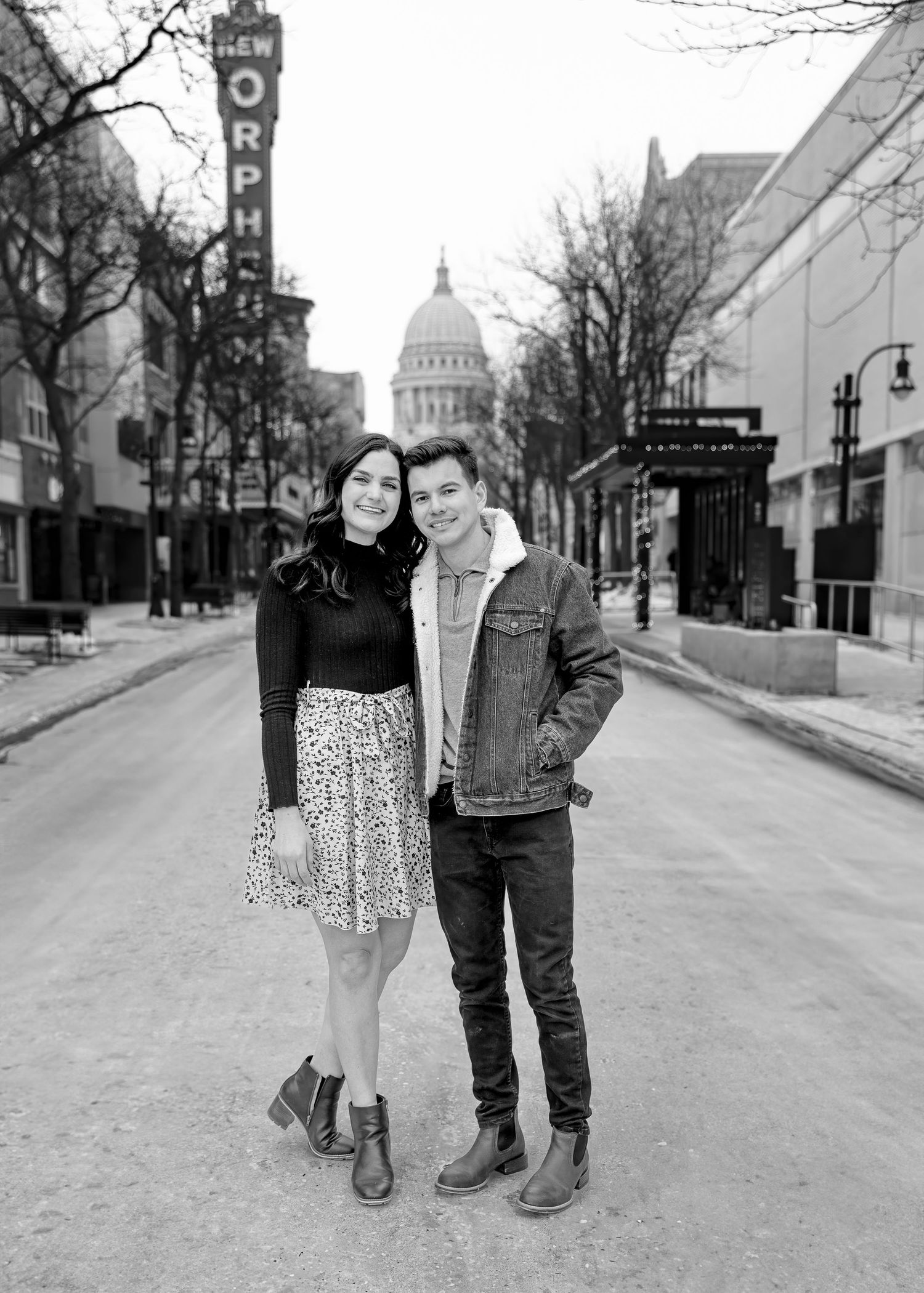 Couple poses on a snowy urban street near the New Orpheum Theatre and capitol building.
