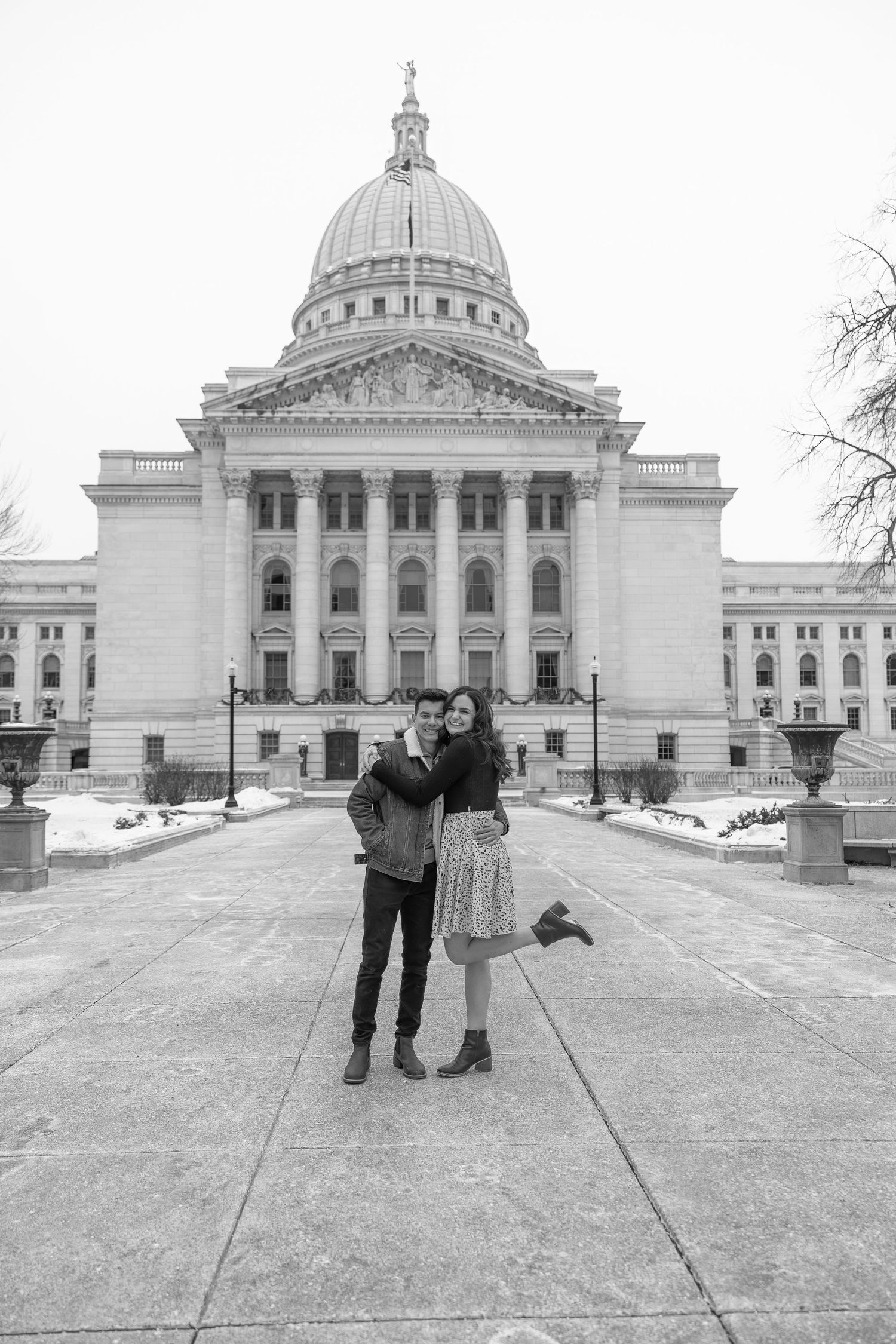 Black and white photo of couple embracing in front of a grand domed capitol building in winter.