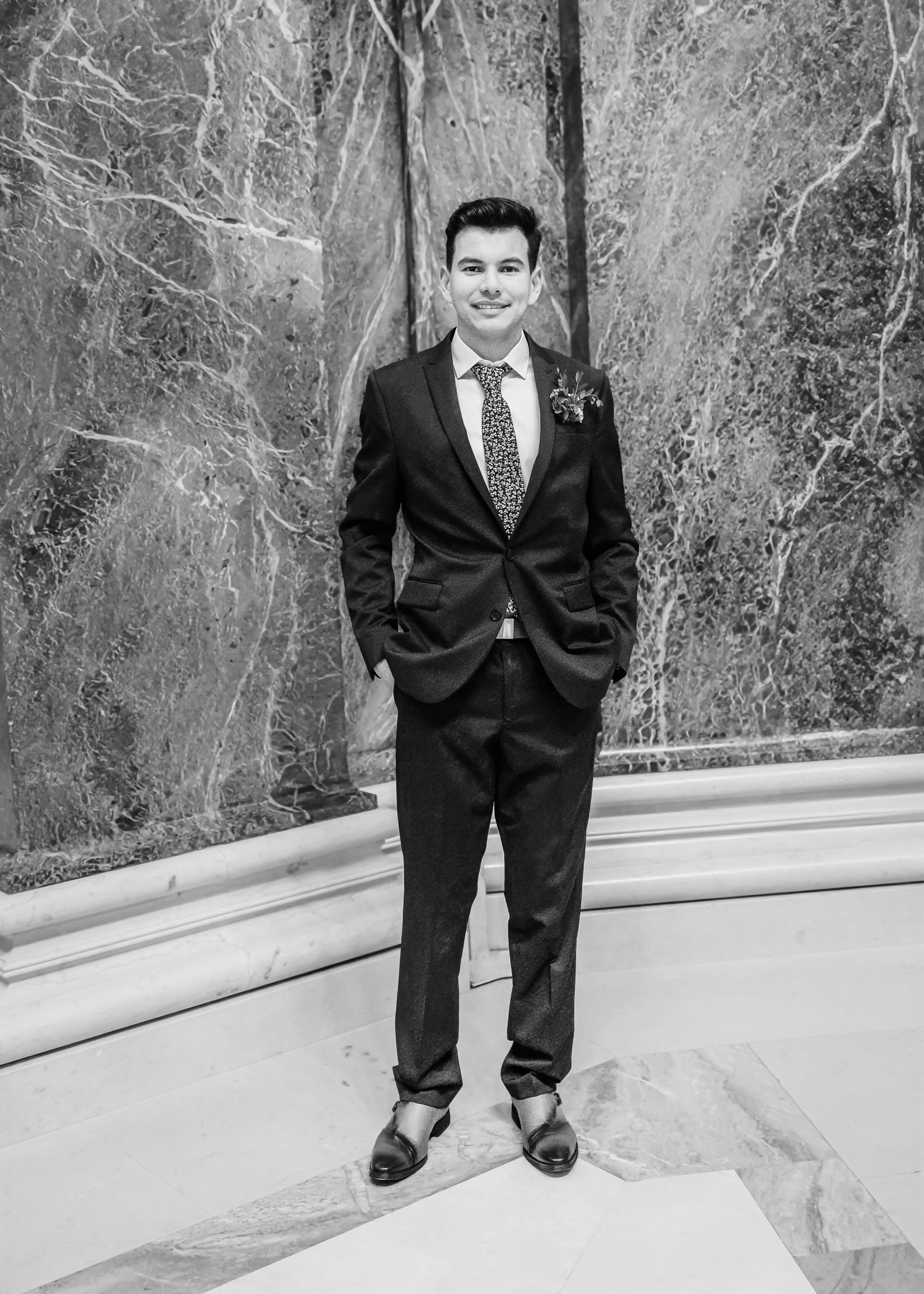 Dapper groom poses solo in black and white portrait wearing suit with floral boutonniere.