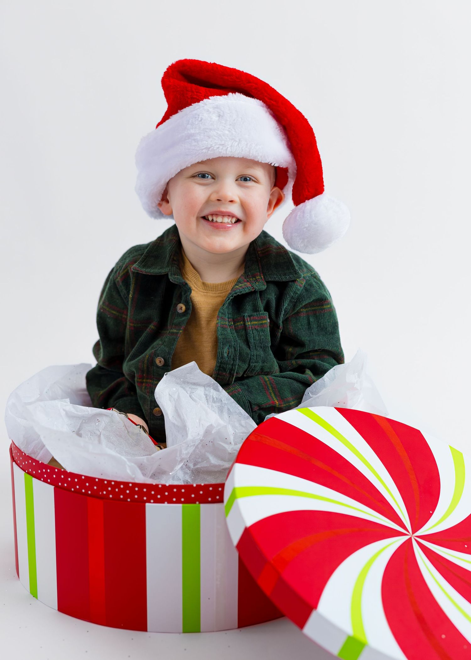 Cheerful child in Santa hat smiling while sitting inside large festive Christmas gift box.