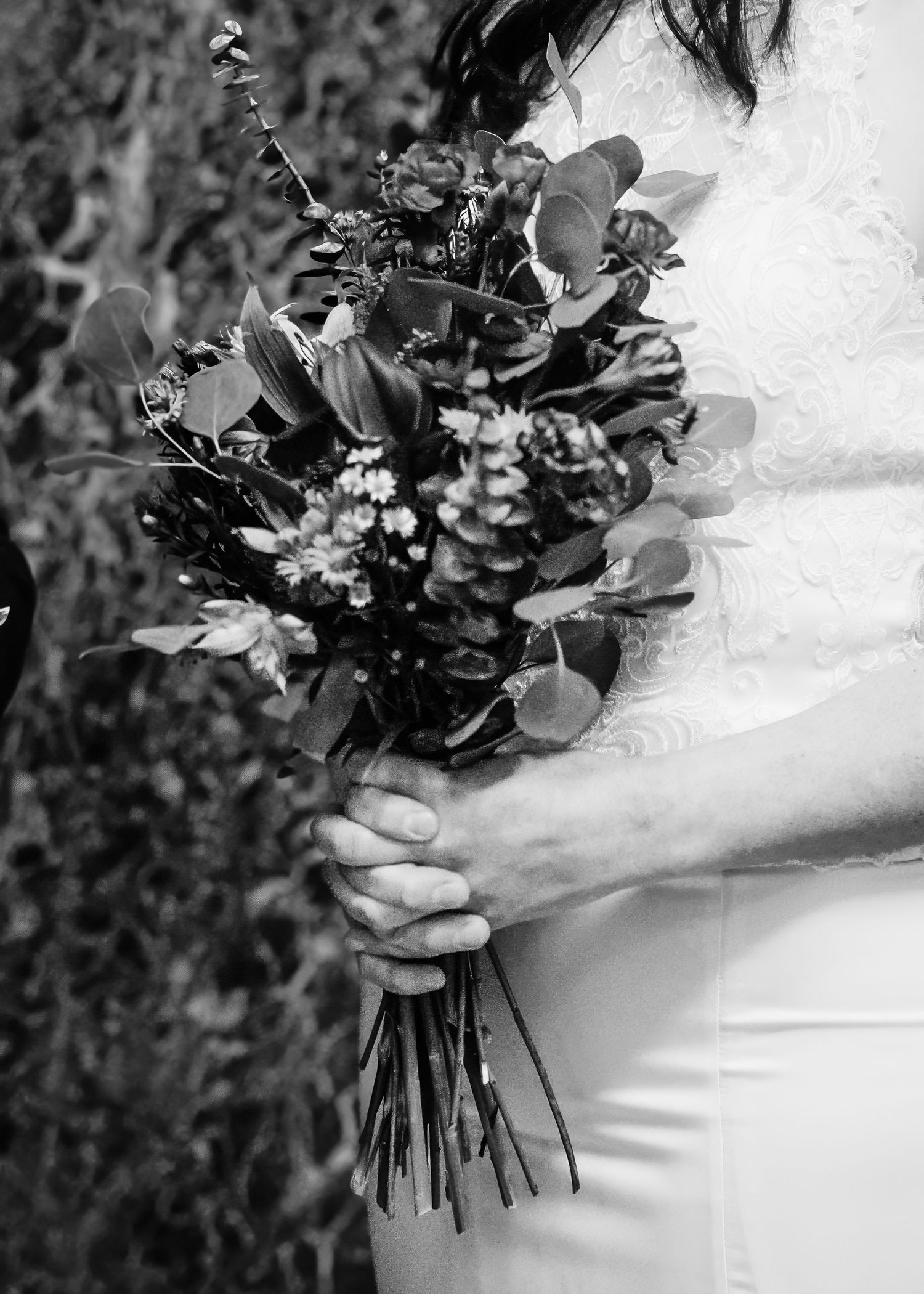 Close-up of bride holding rustic wildflower bouquet with eucalyptus in white lace wedding gown.
