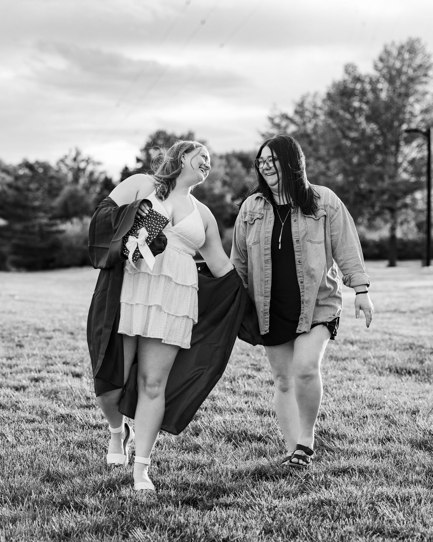 Two women laughing and walking together on grass in black and white photo outdoors.