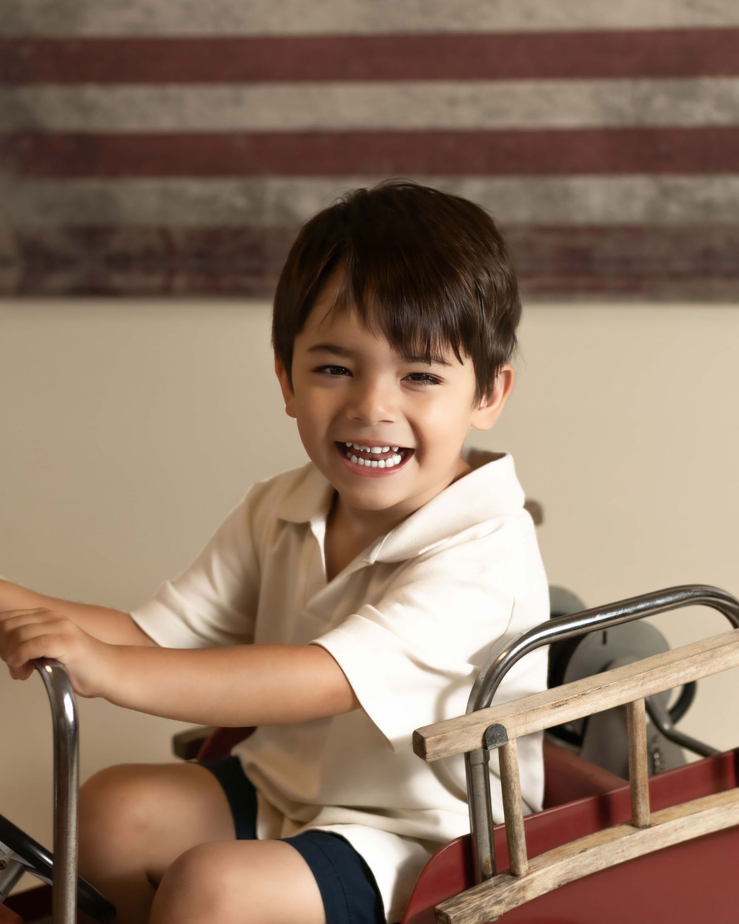 Happy young boy laughing while sitting in a vintage red pedal fire truck.