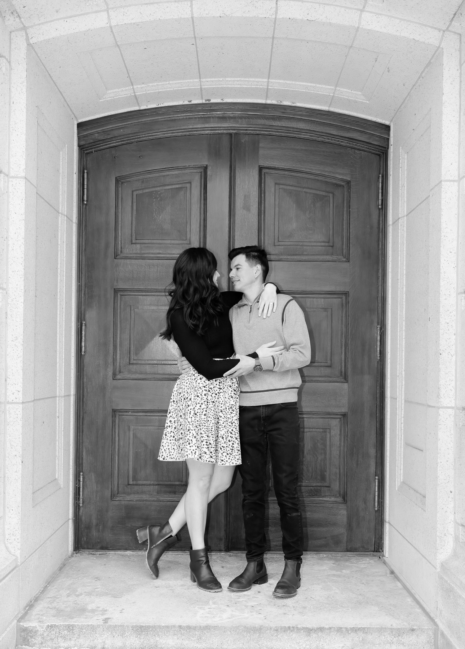 Black and white photo of couple facing each other romantically in front of large wooden double doors.