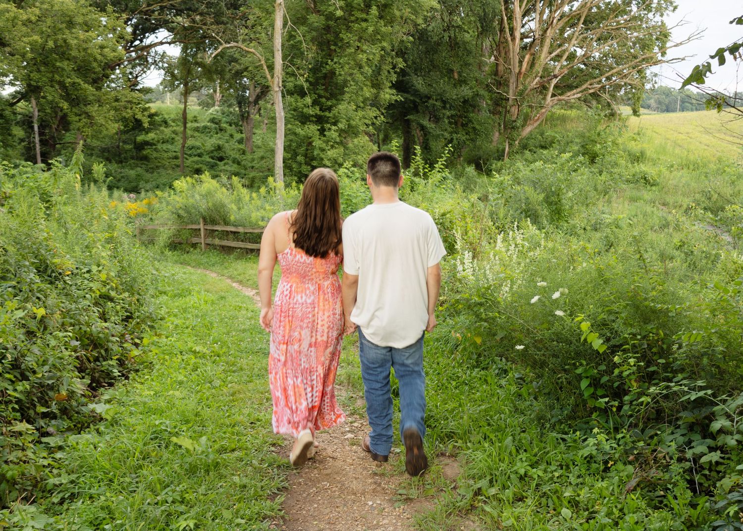 Young couple walking hand in hand along a scenic green nature trail surrounded by lush foliage.