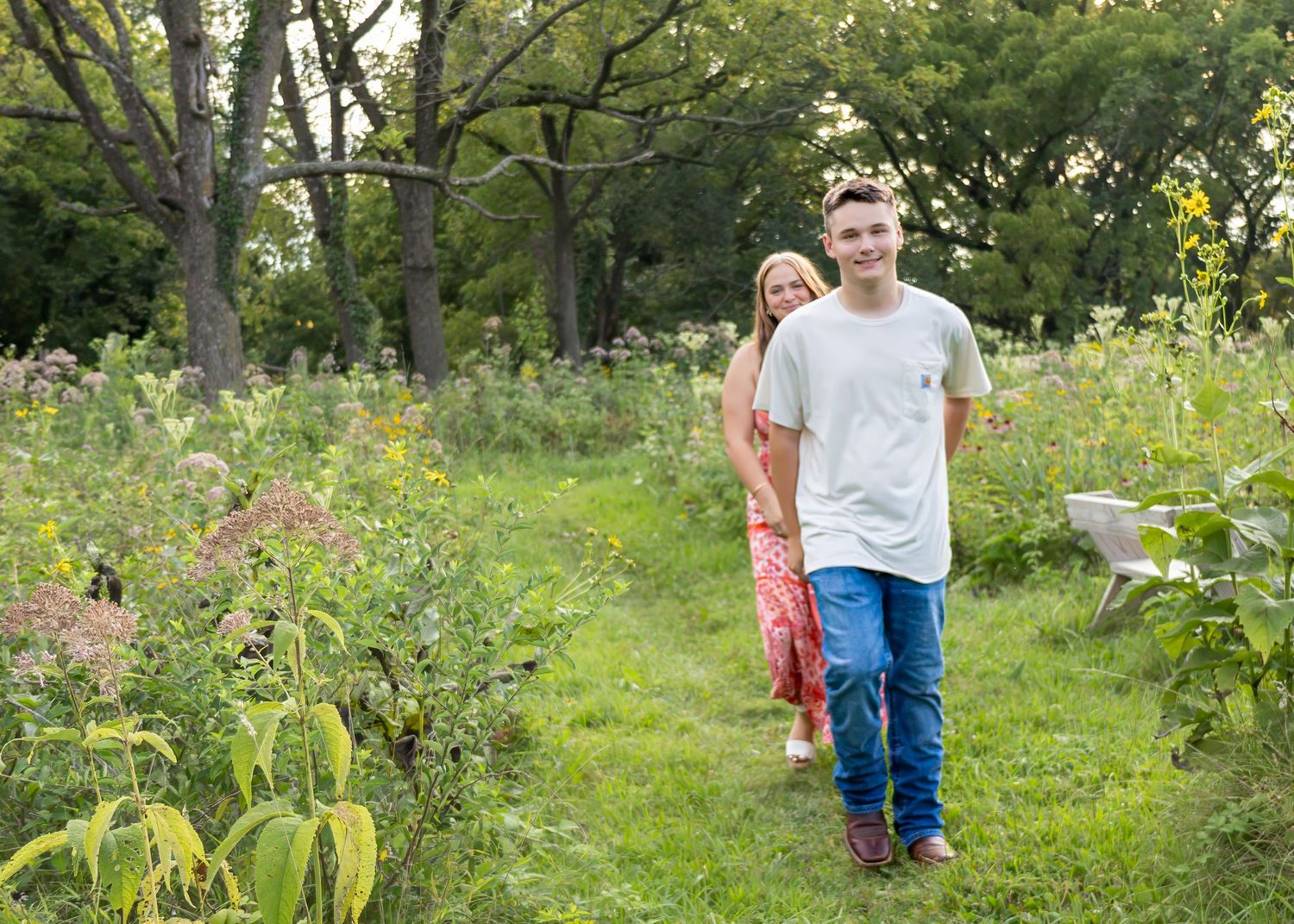 Teen boy and girl walking along a wildflower garden path surrounded by lush greenery.