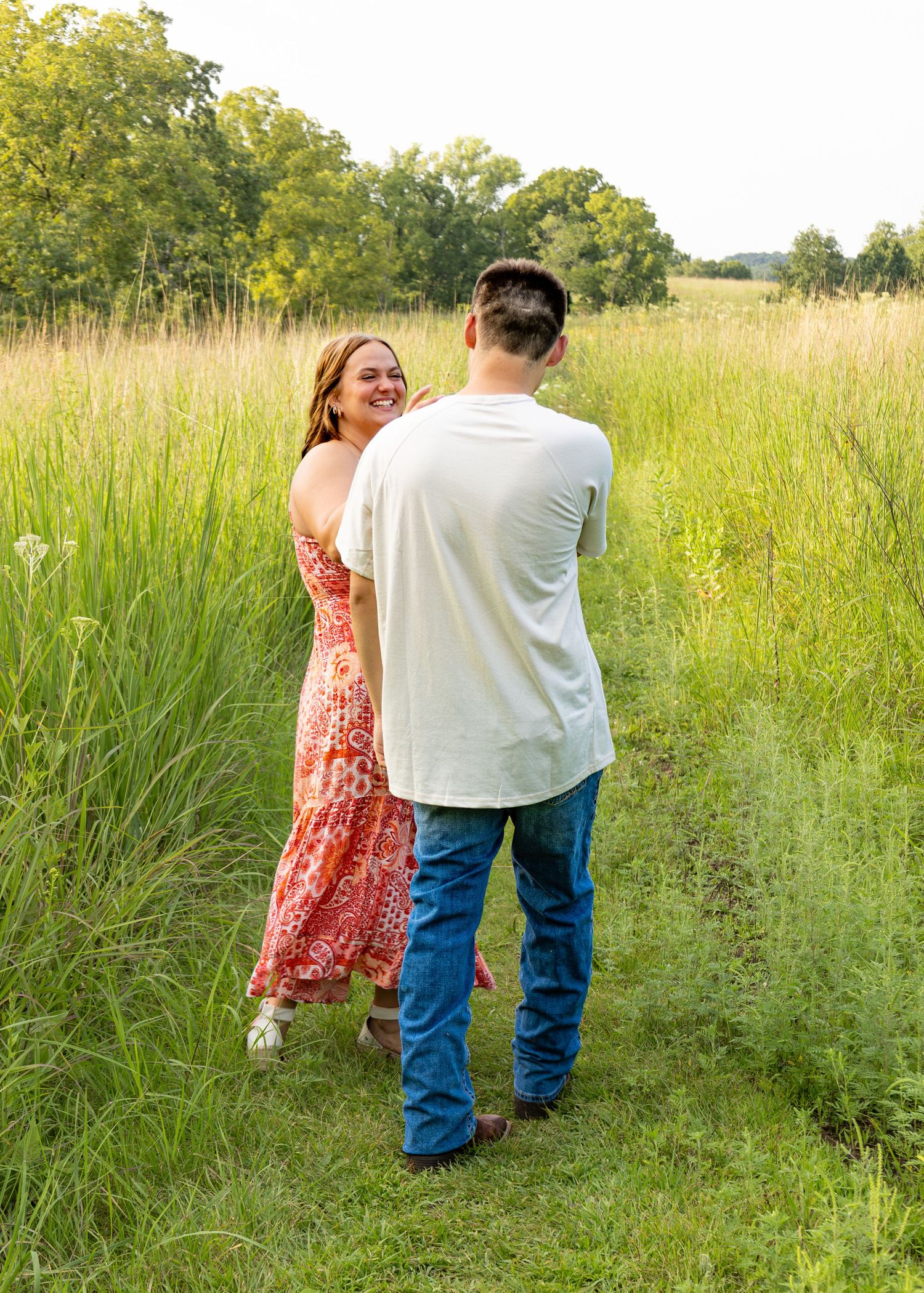 A smiling woman glances back while her partner leads her by the hand through a green meadow.