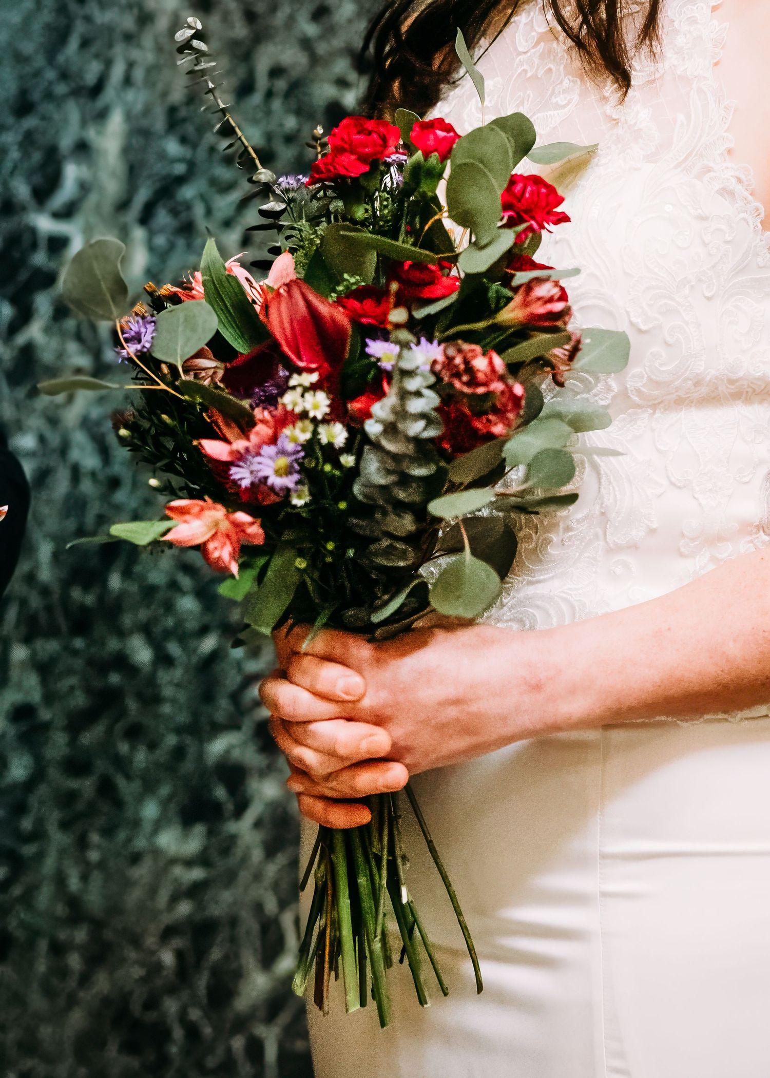Close-up of bridal bouquet with red roses, lilies, and eucalyptus greenery.