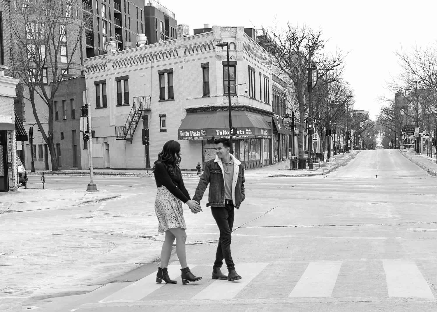 Black and white photo of couple holding hands while crossing an empty urban intersection.
