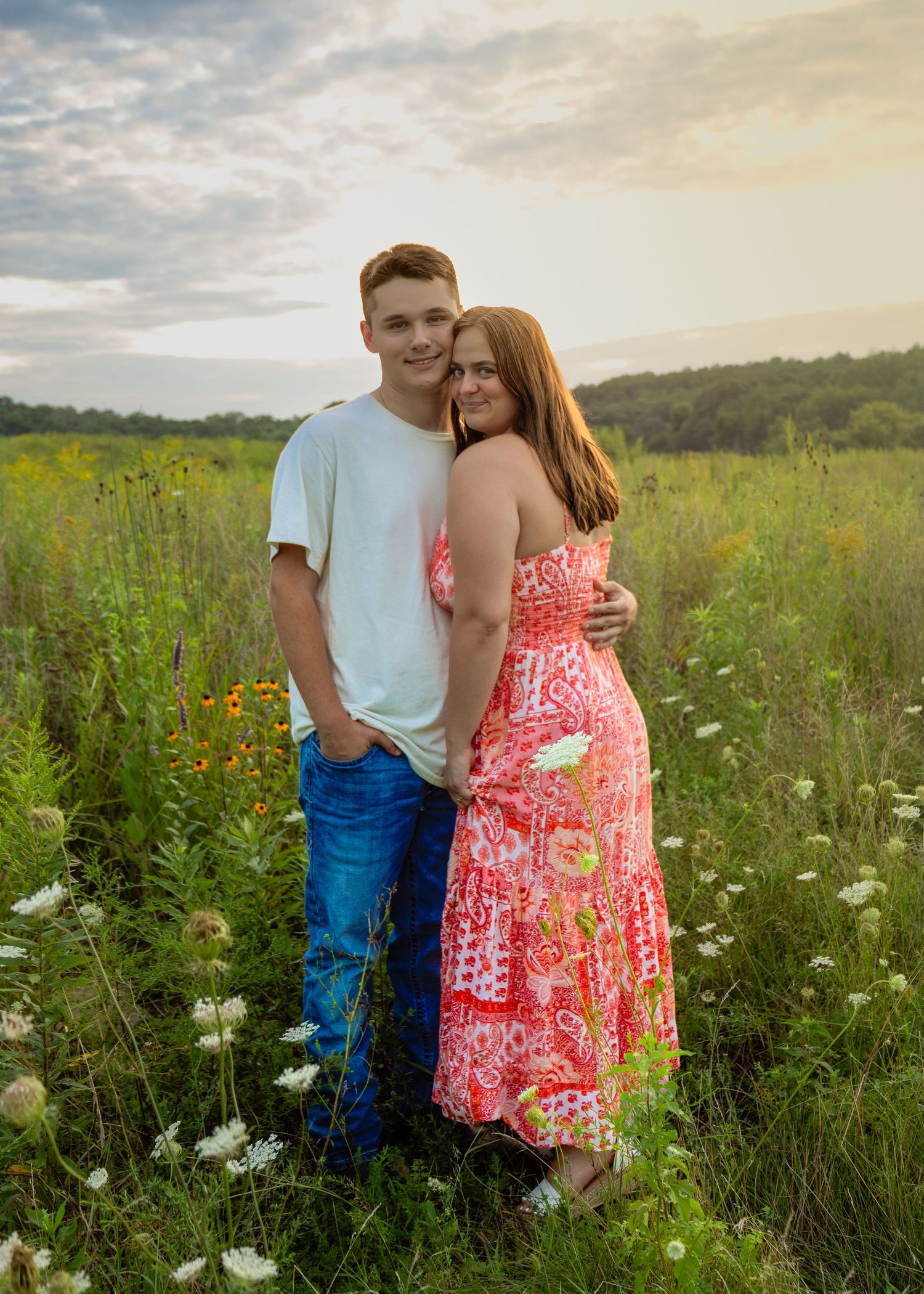 A young couple embracing in a sunlit wildflower meadow during a golden hour outdoor photo session.