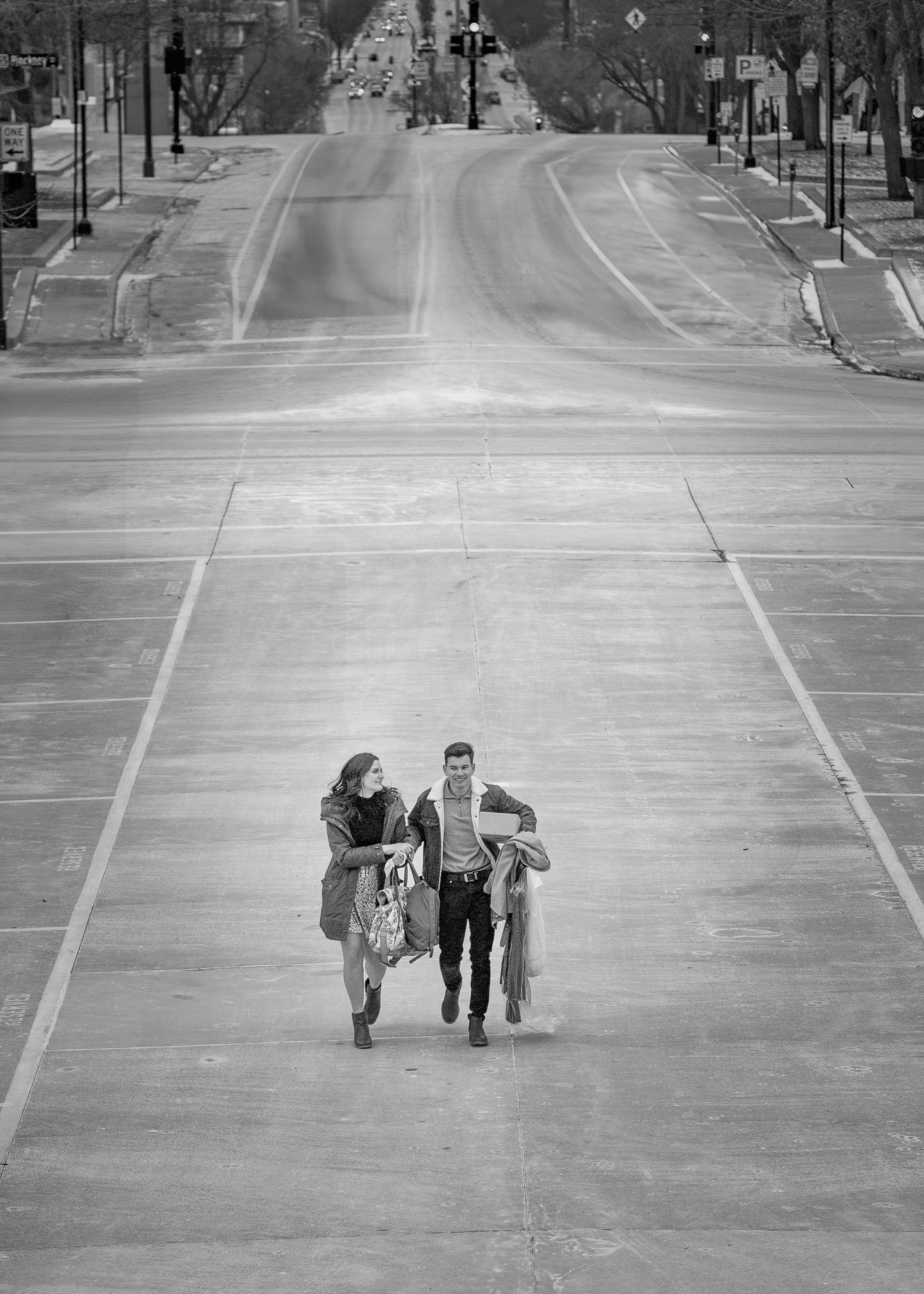 Black and white aerial view of couple walking up empty urban street toward grand building.