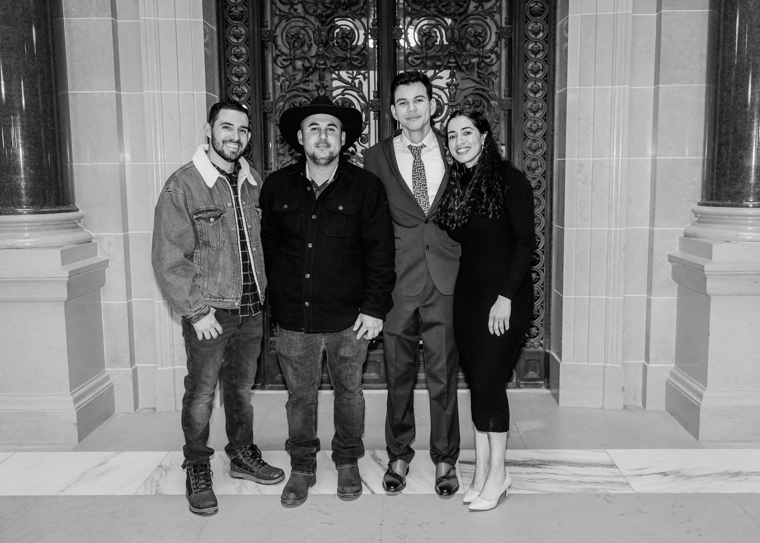 Black and white photo of four wedding guests posing in front of ornate doors at a city hall venue.