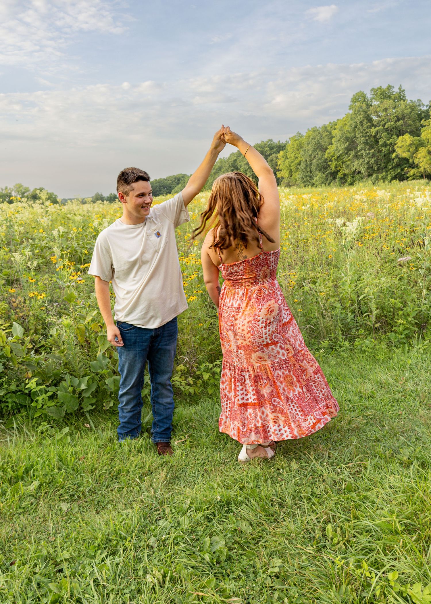 Couple twirling together in a lush green field with yellow wildflowers at sunset.