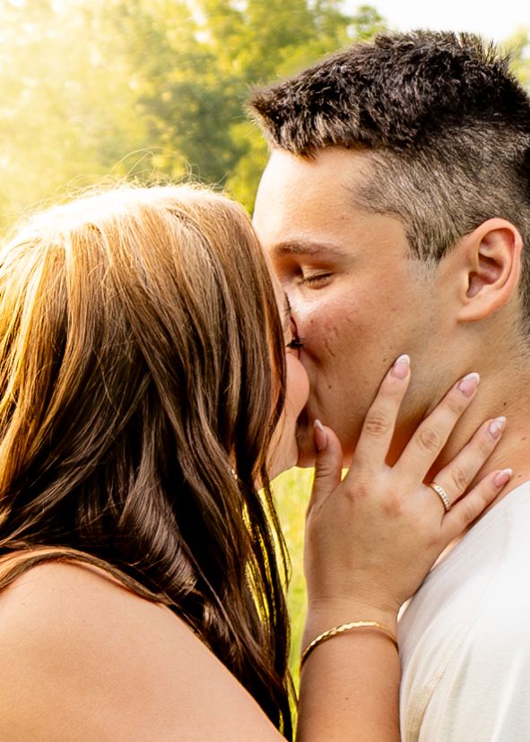 Close-up of couple sharing a tender kiss outdoors with soft golden sunlight in the background.